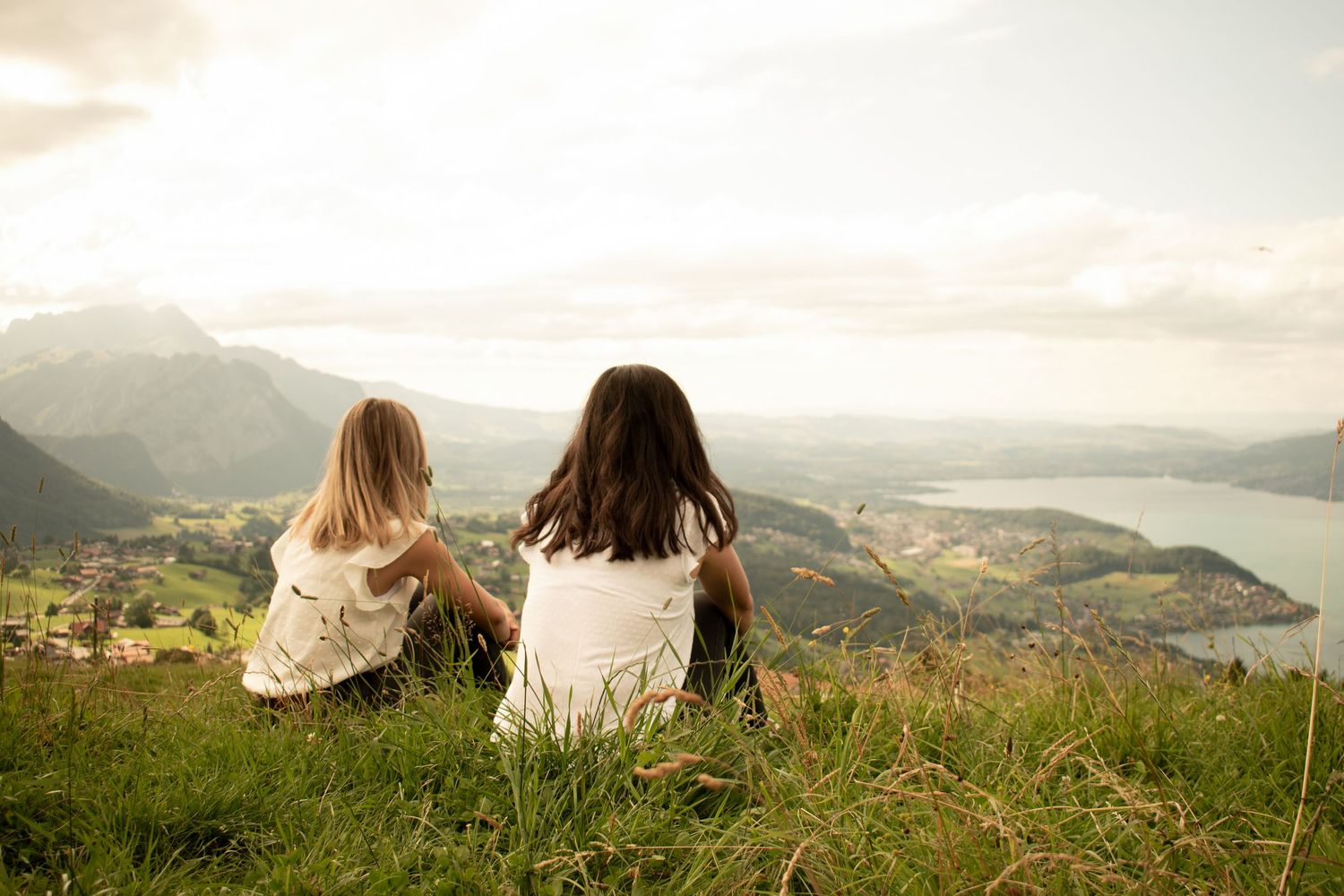 Group sitting together on grassy hilltop overlooking scenic mountain valley at sunset.