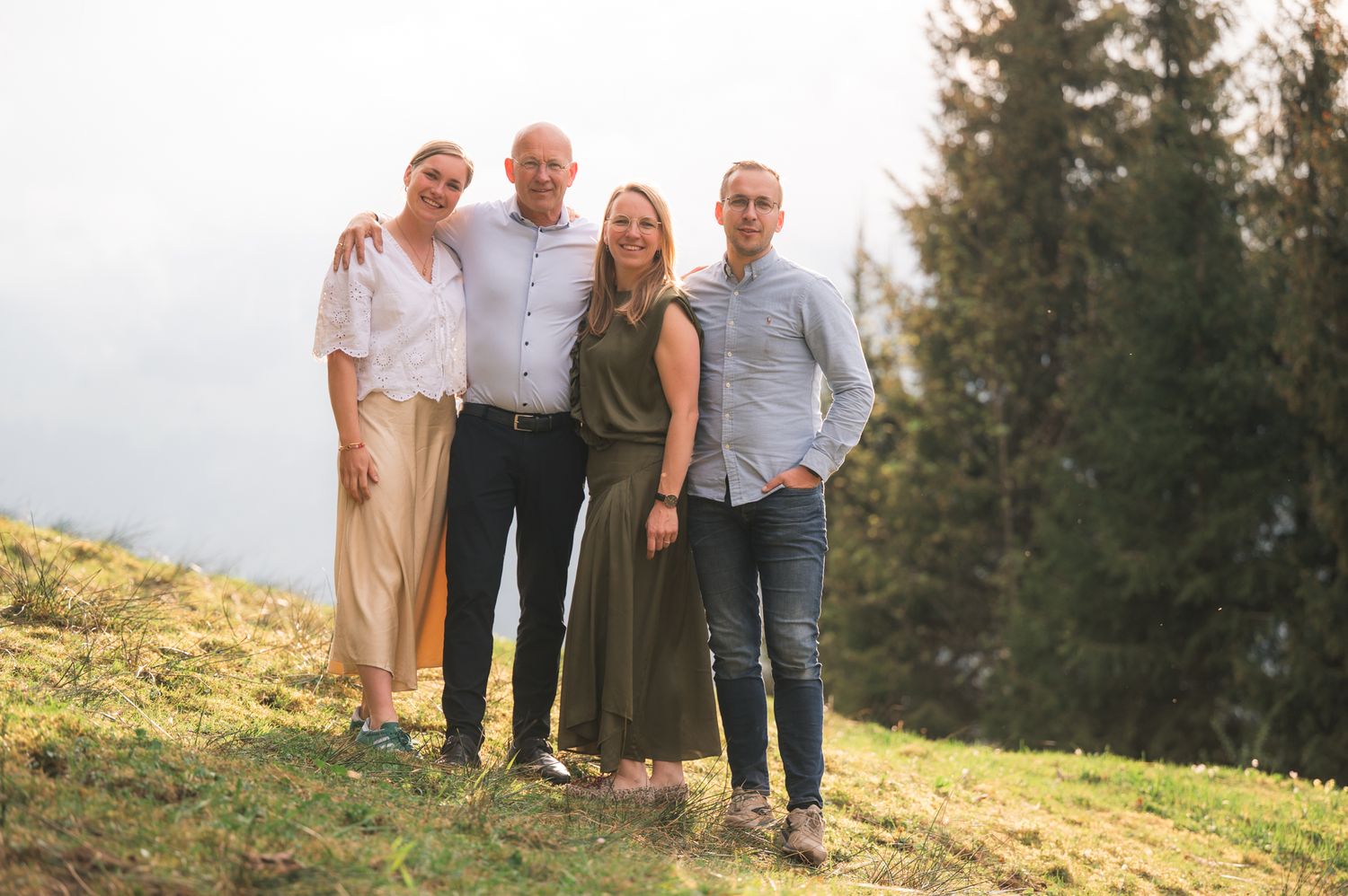 Four adults posing together on a grassy hillside with a misty mountain backdrop during golden hour.