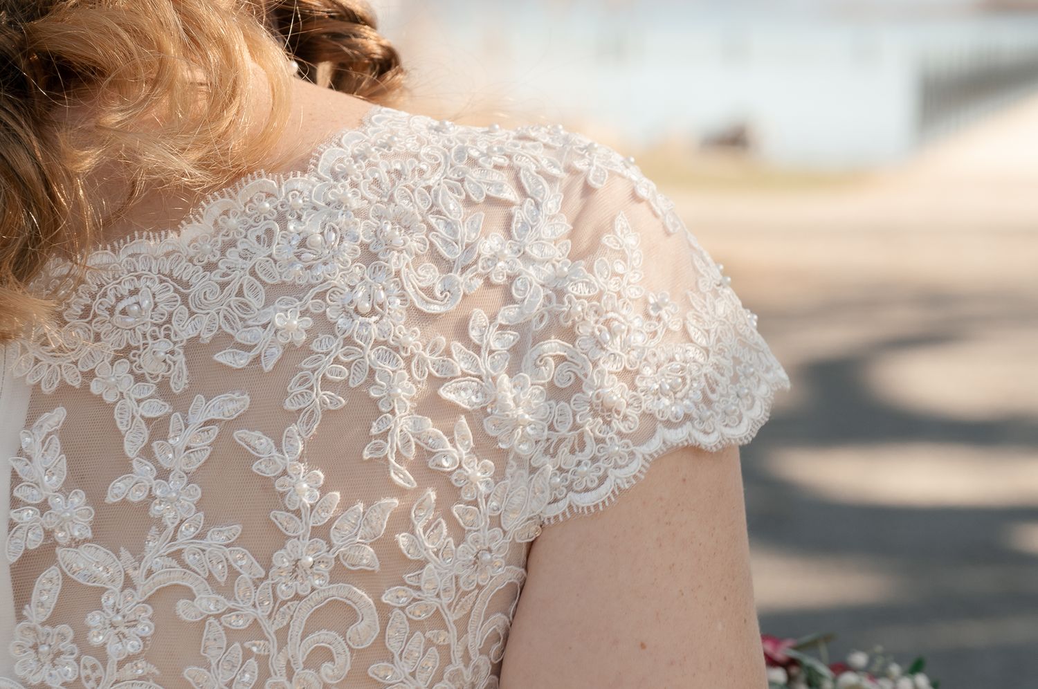 Close-up details of delicate white lace embroidery and beadwork on wedding dress fabric.