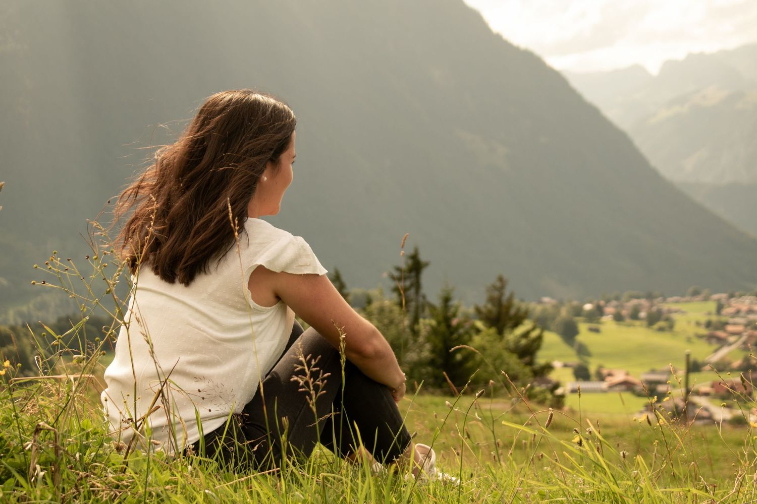 Person sitting thoughtfully on mountainside overlooking scenic alpine valley.