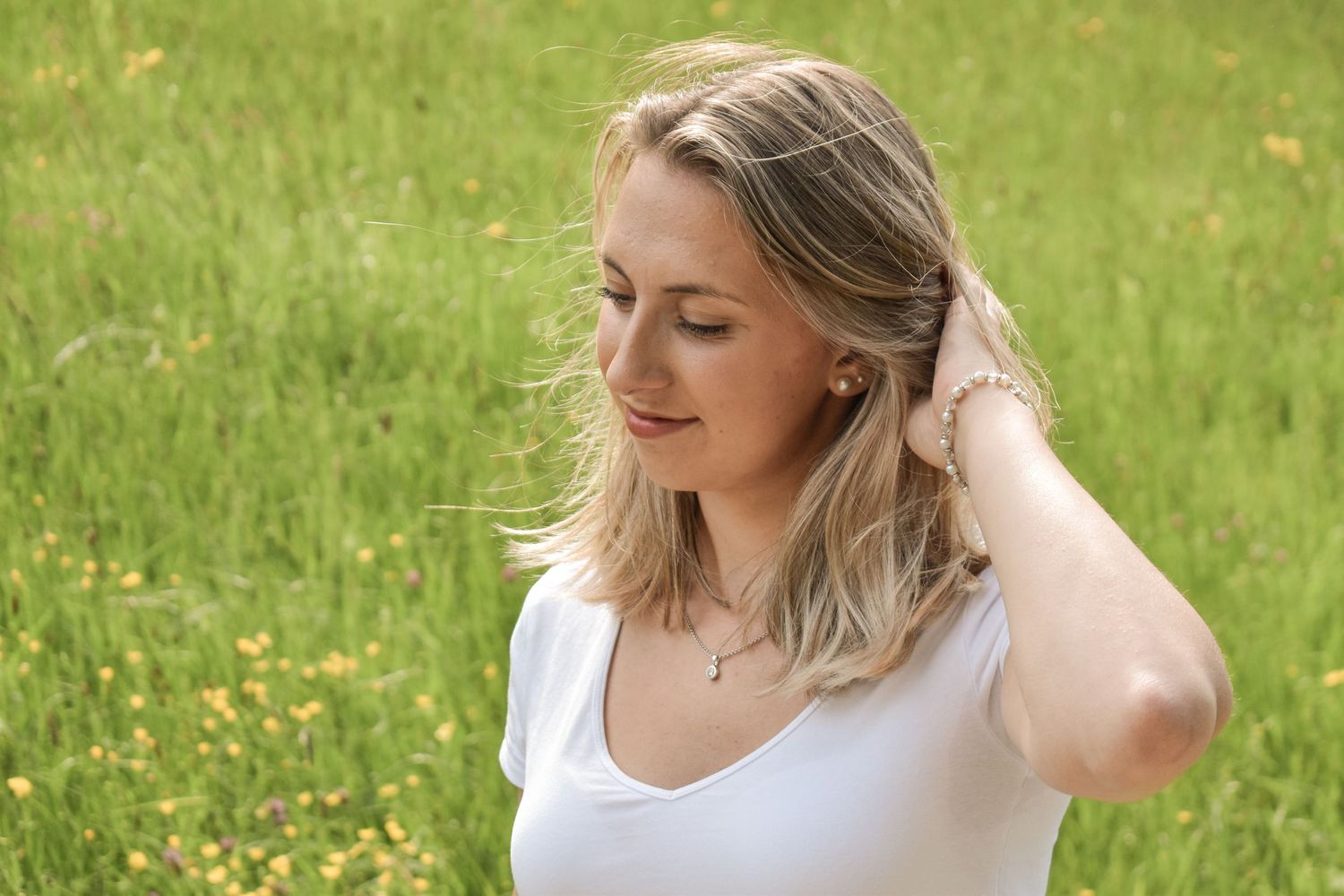 Woman in white top sitting outdoors in green grass field on sunny day.