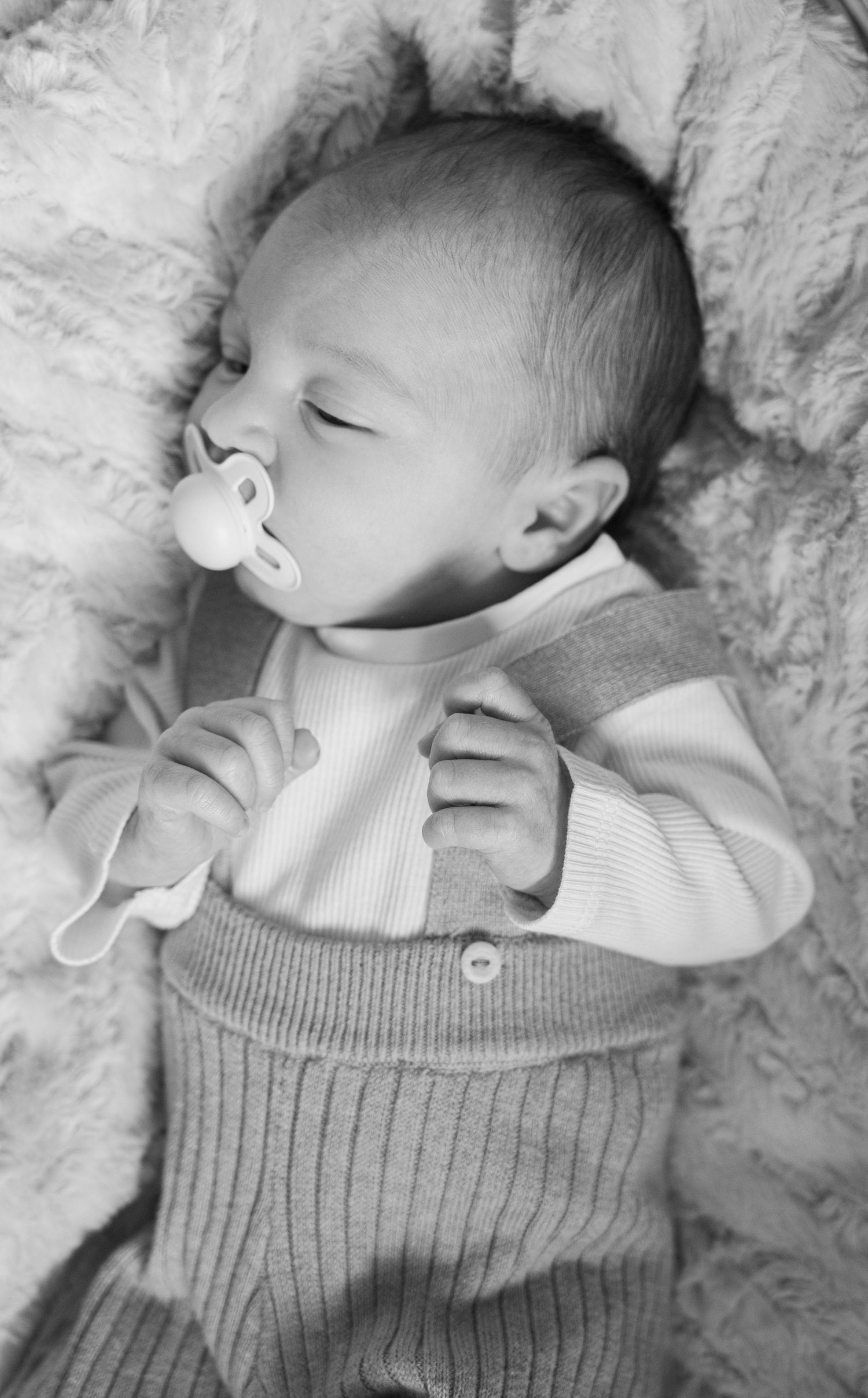 Peaceful newborn sleeping in a white knit sweater against a plush white background.