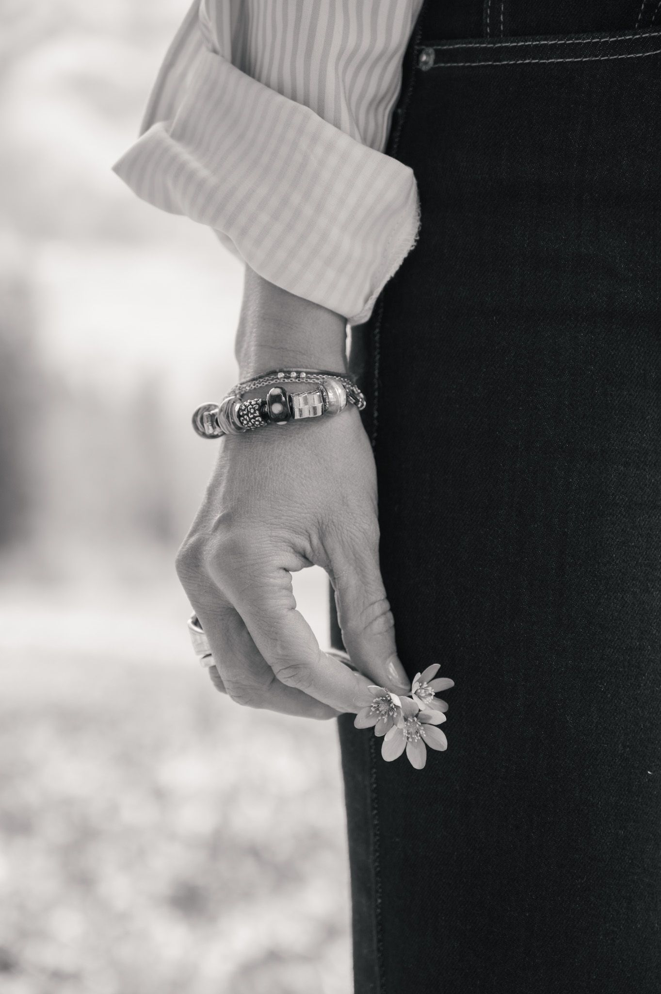 A close-up black and white photo of hands wearing a delicate flower ring against a dark background.