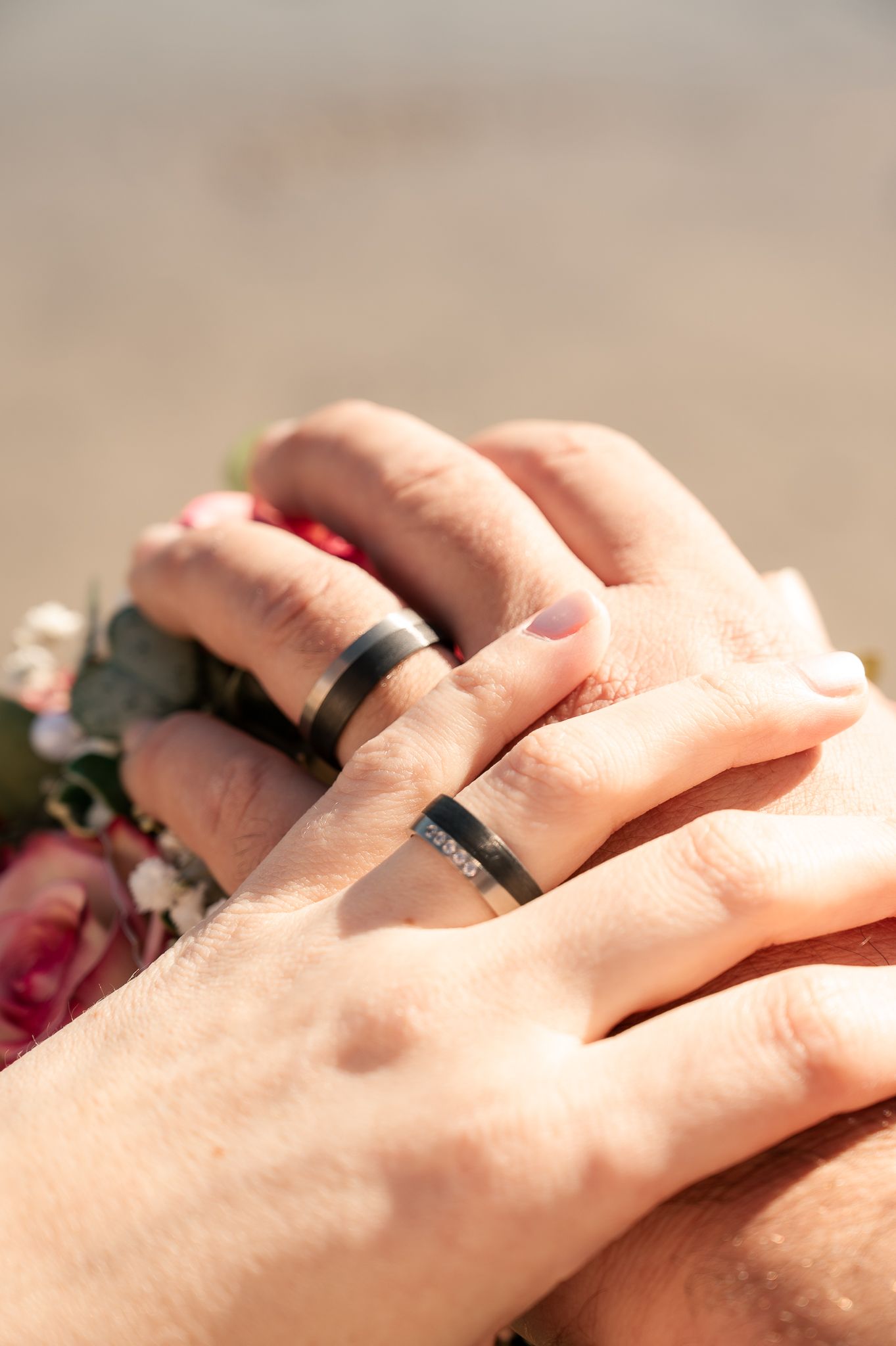 Close-up view of hands wearing matching black silicone wedding rings in natural sunlight.