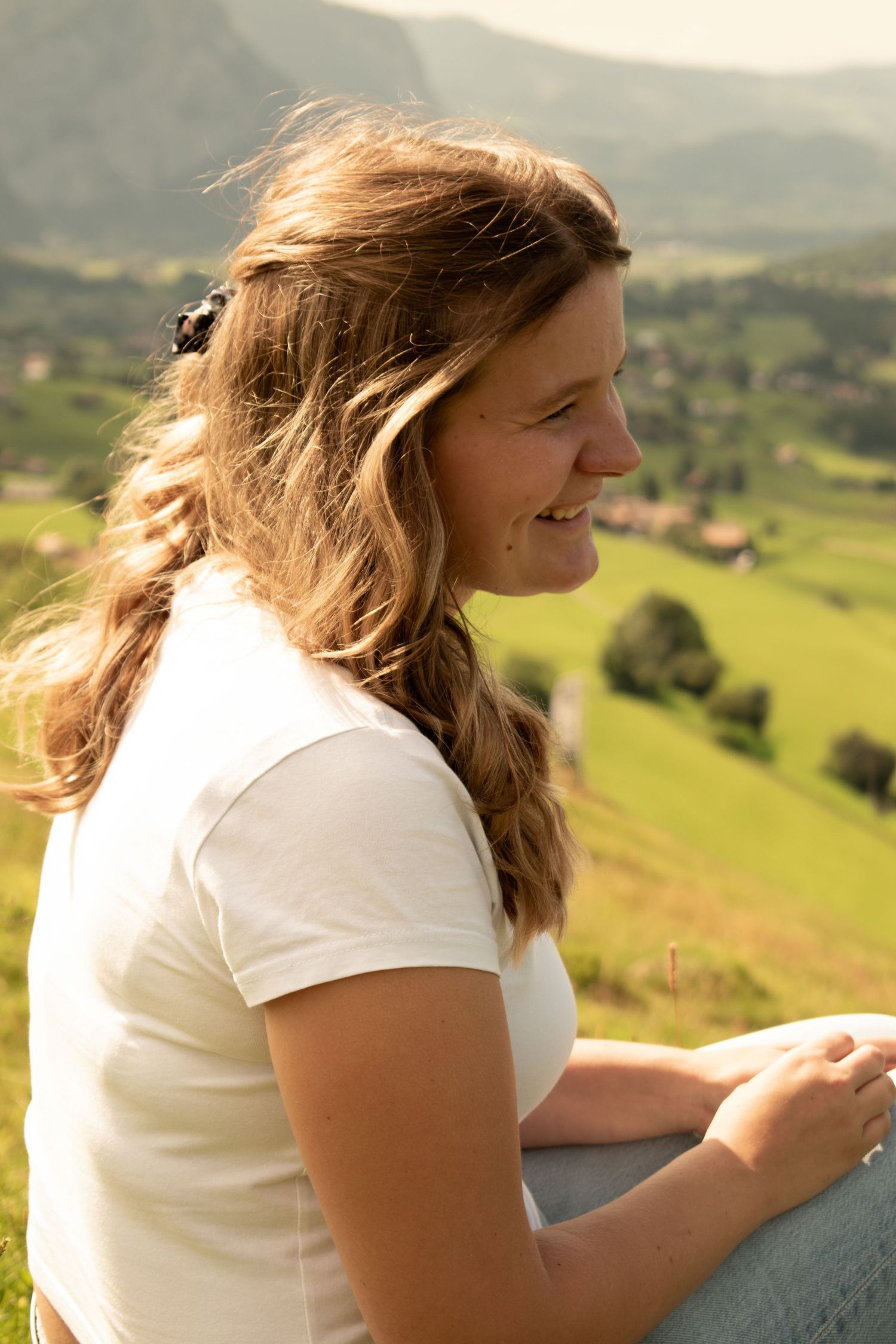 Relaxed figure sitting on hillside overlooking scenic mountain valley in summer.