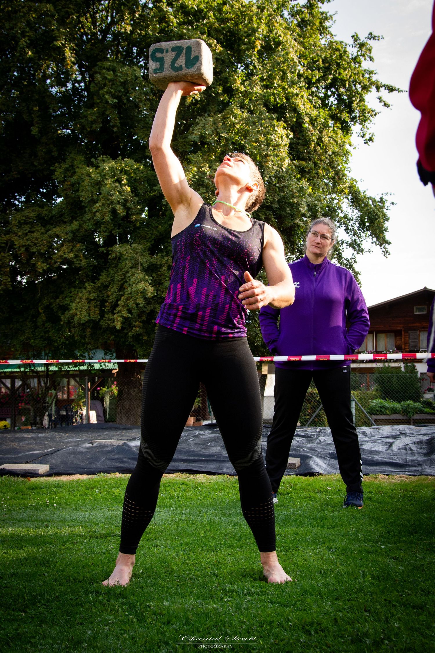 People in purple shirts performing synchronized dance moves on grass field.