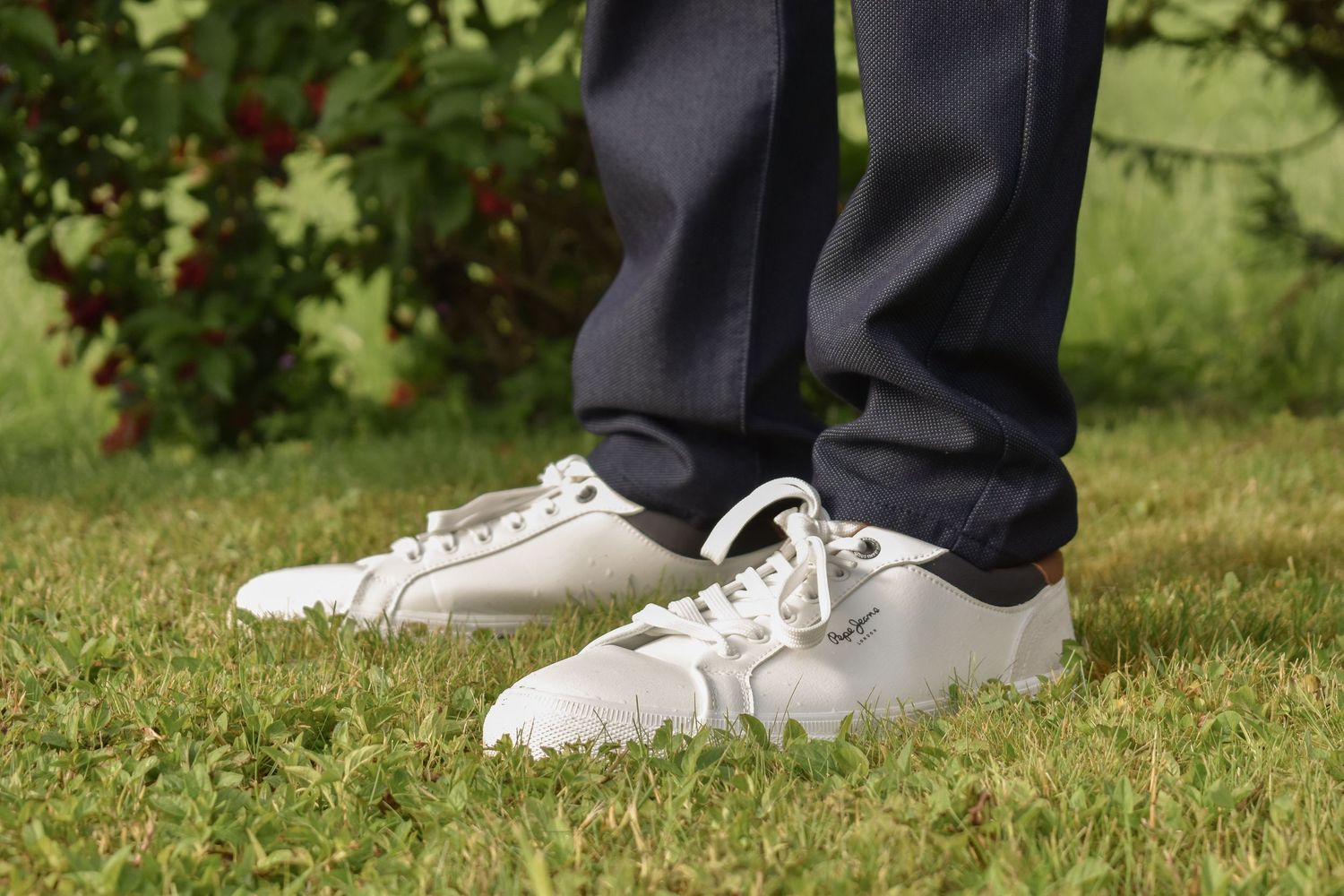 White sneakers and dark pants standing on green grass.