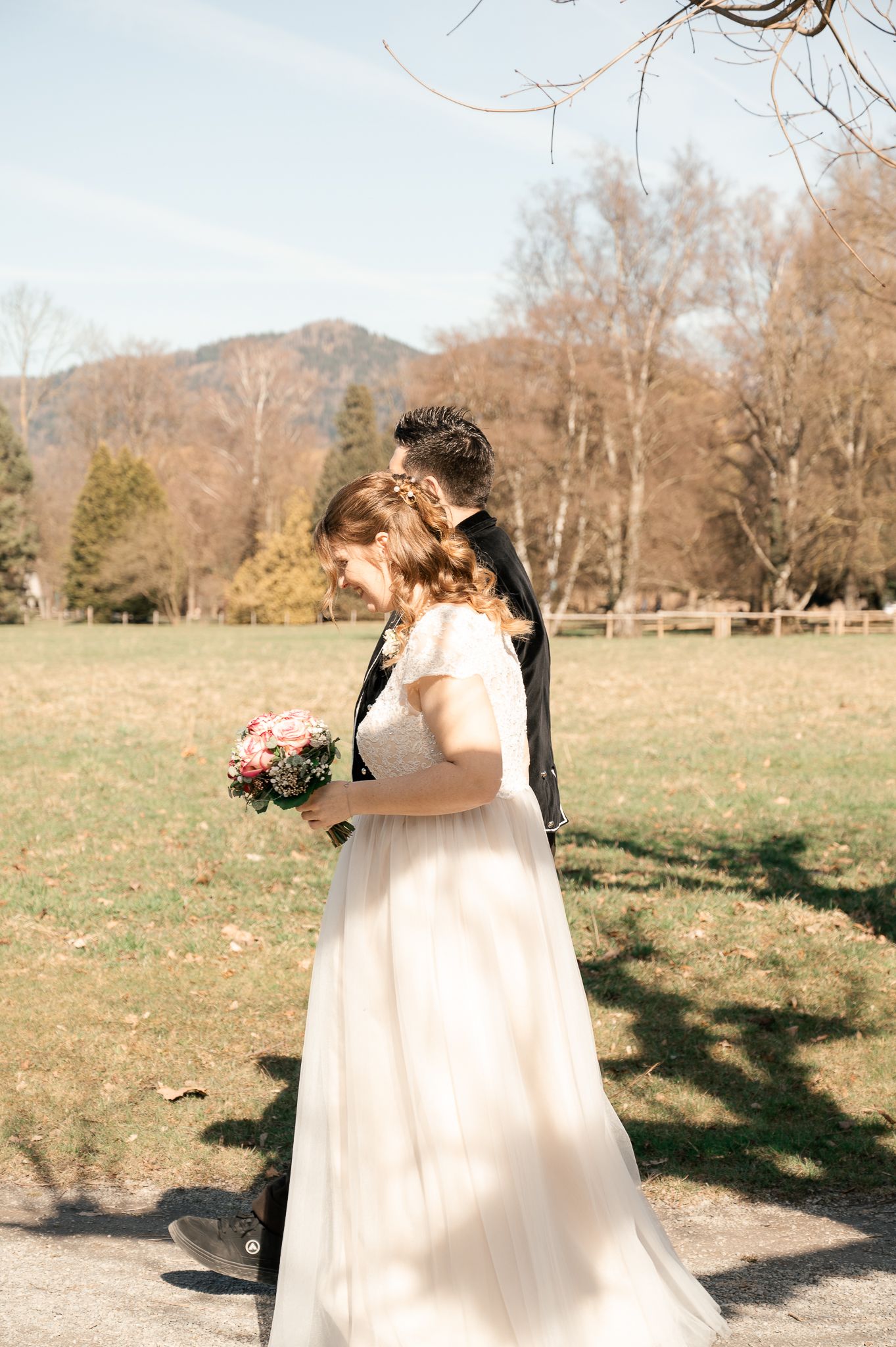 A couple shares an intimate moment in a flowing white dress against a scenic mountain backdrop on their wedding day.