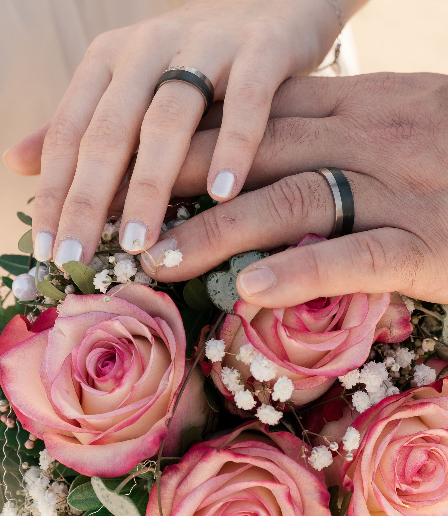 Close-up of hands arranging pink roses and baby's breath flowers in a floral arrangement.