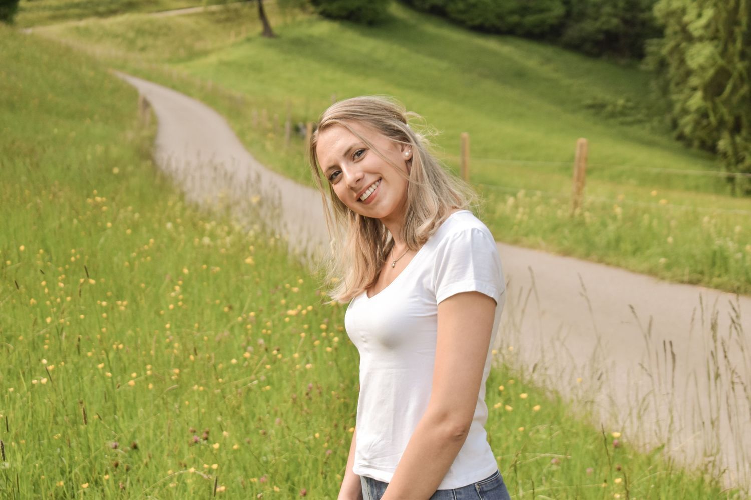 Person walking on a winding path through a sunny green meadow with wildflowers.