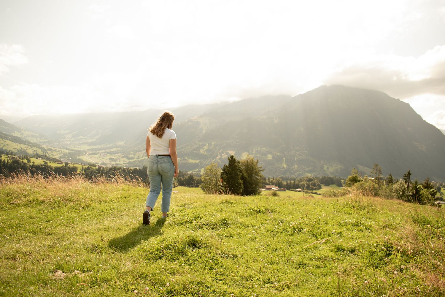 Person walking across scenic mountain meadow at sunset.