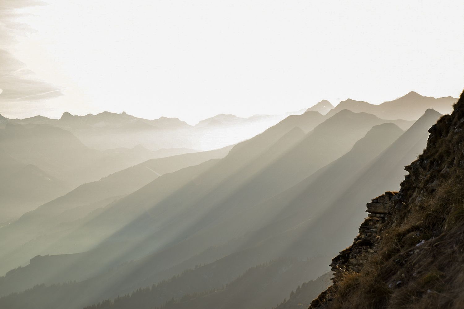 Dramatic sunbeams streaming through mountain ridges creating layers of misty silhouettes.