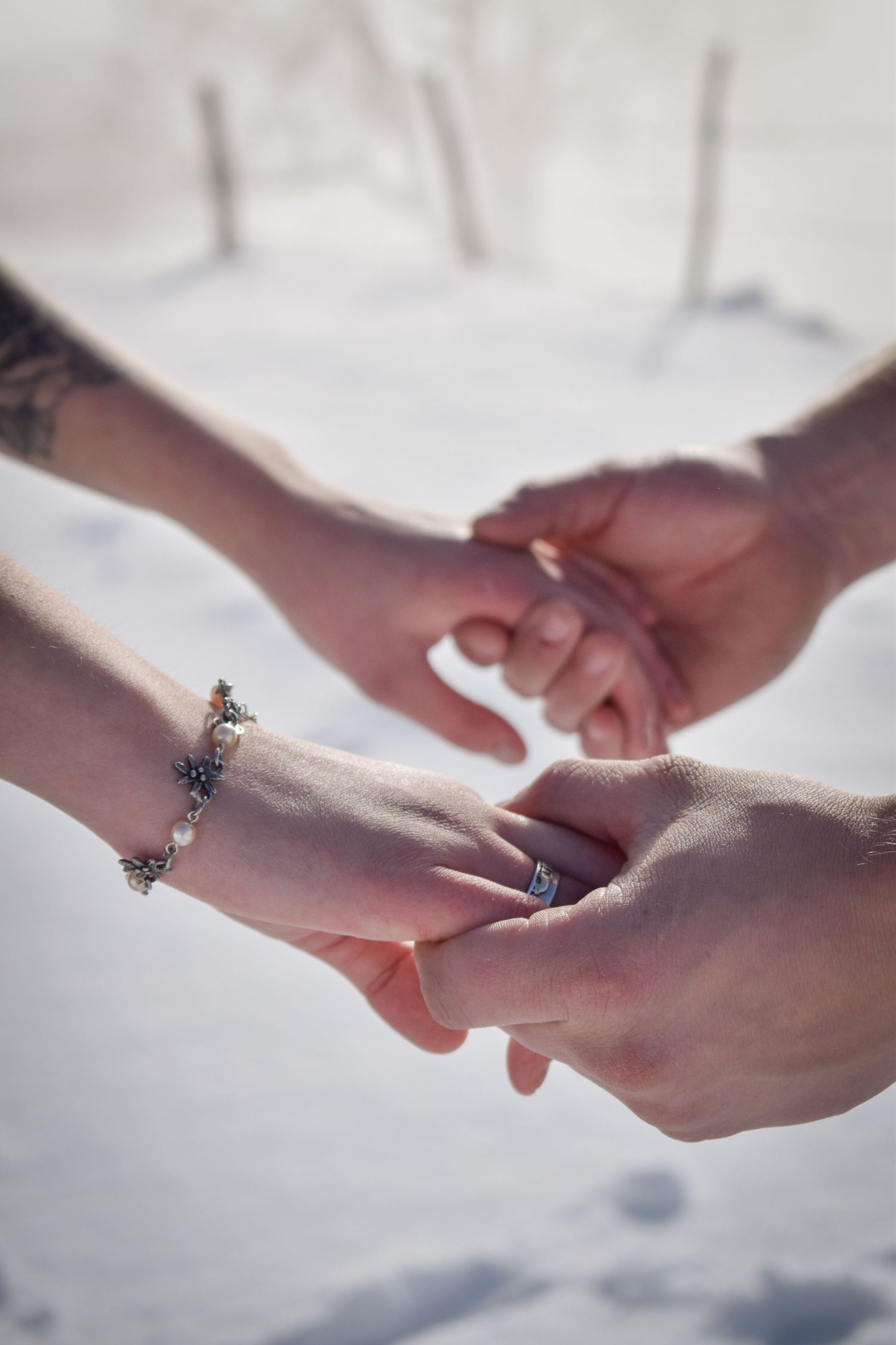 Close-up of hands with rings gently touching against a bright white background.