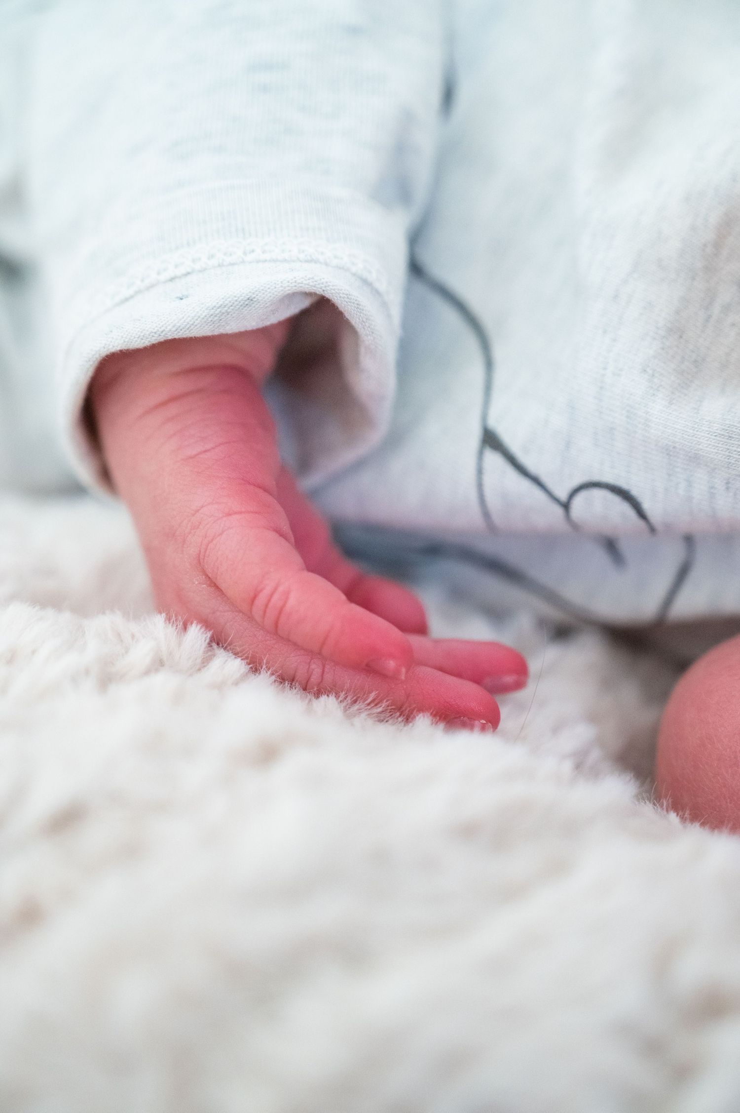 Close-up of tiny baby fingers against soft white fabric background.
