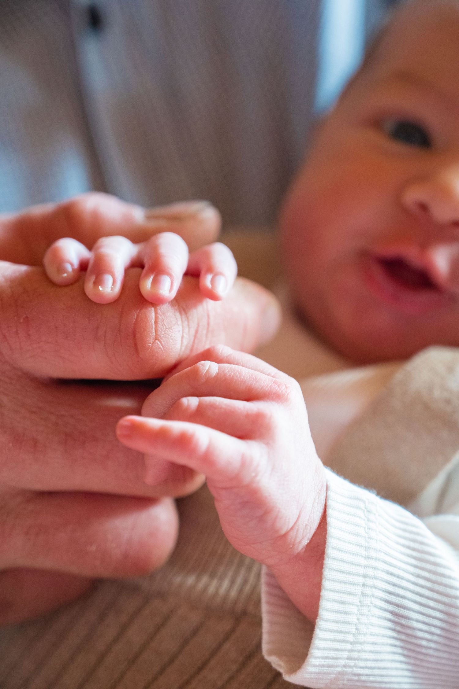 Delicate baby hands reaching out while wearing a white knit sweater.