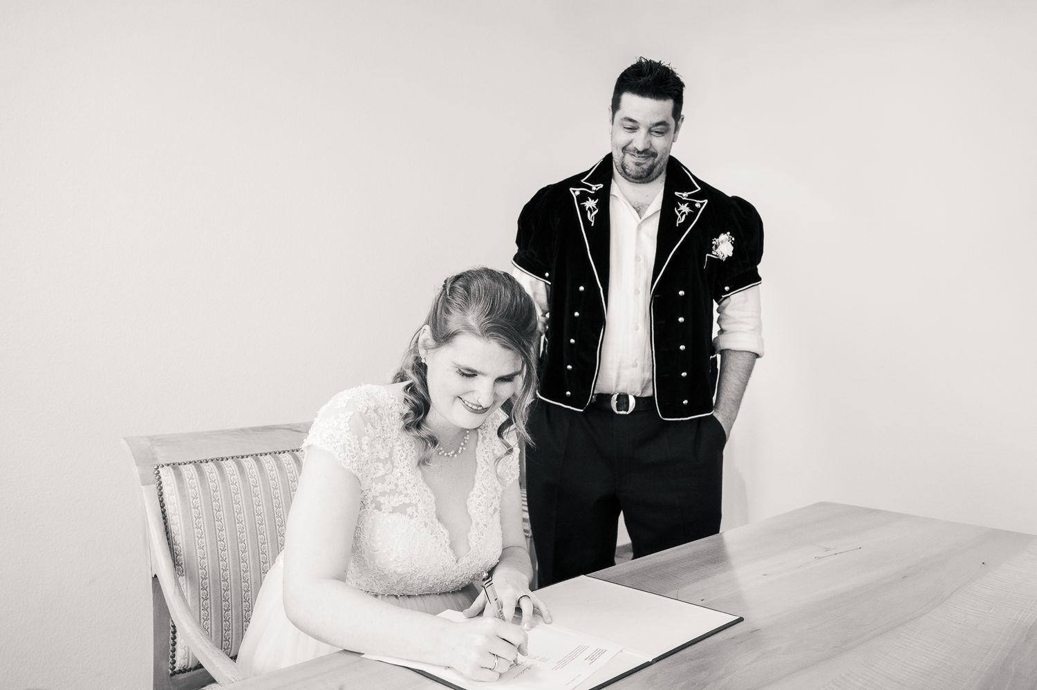 A couple signs their marriage license at a white table during their wedding ceremony.