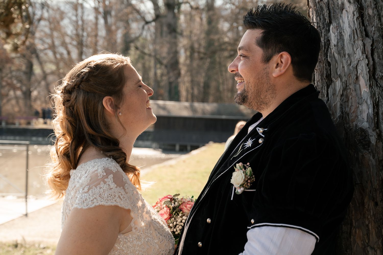 A couple shares a joyful moment together in a sunlit forest setting during their wedding day.