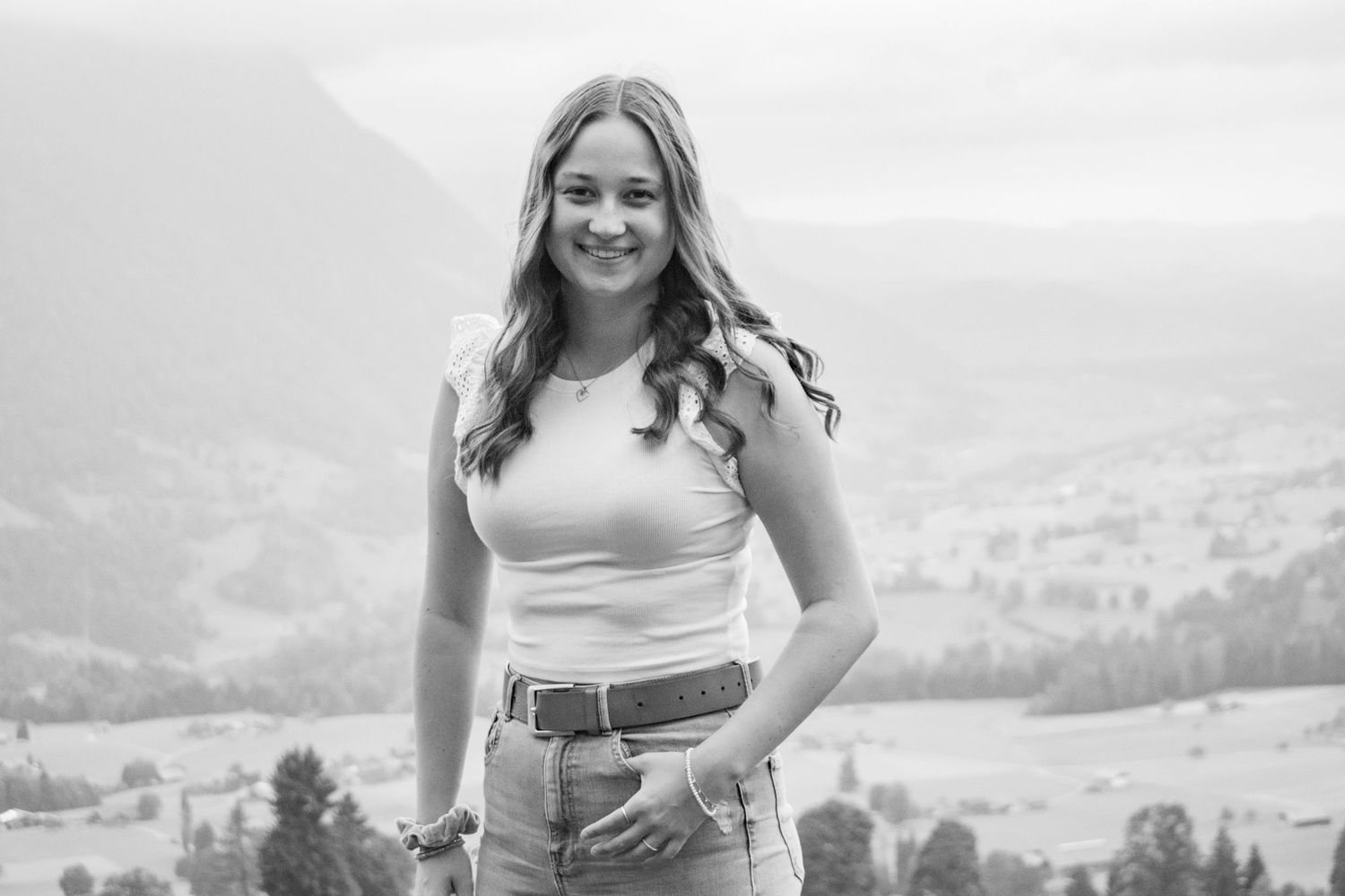 Person posing on hilltop with scenic mountain landscape in black and white.