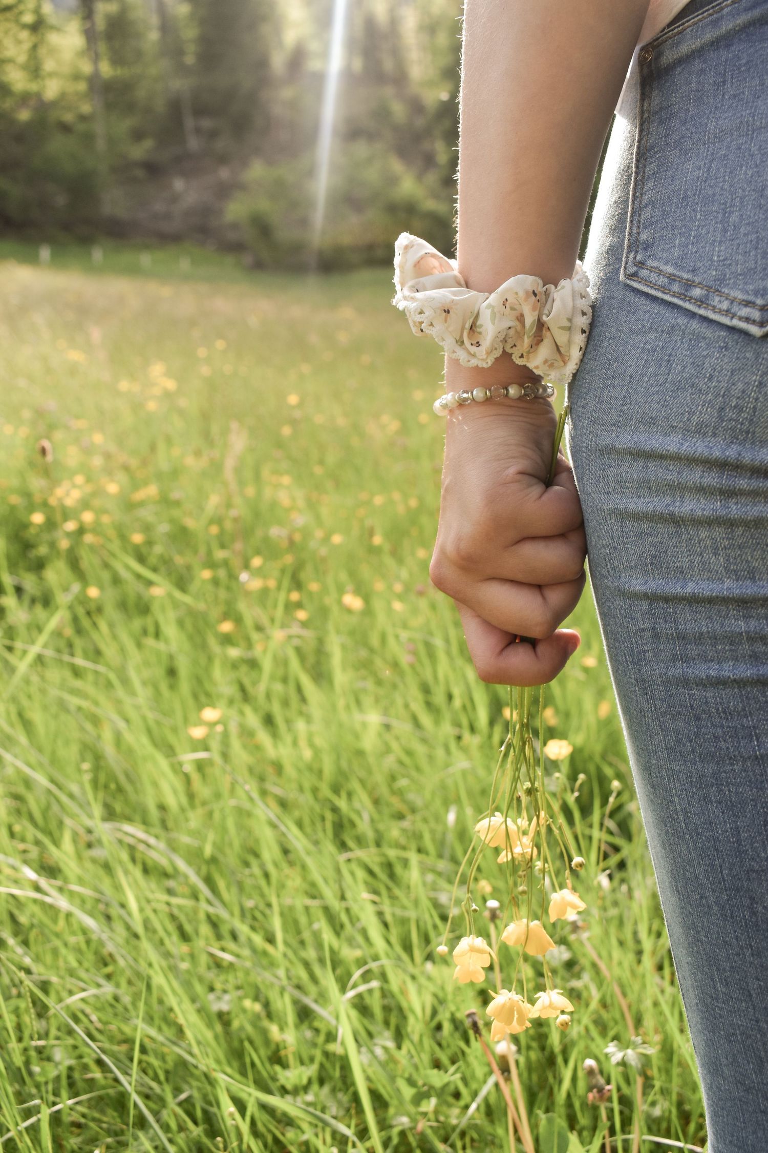 Close-up of hand against blue jeans with green grass and yellow flowers in background.