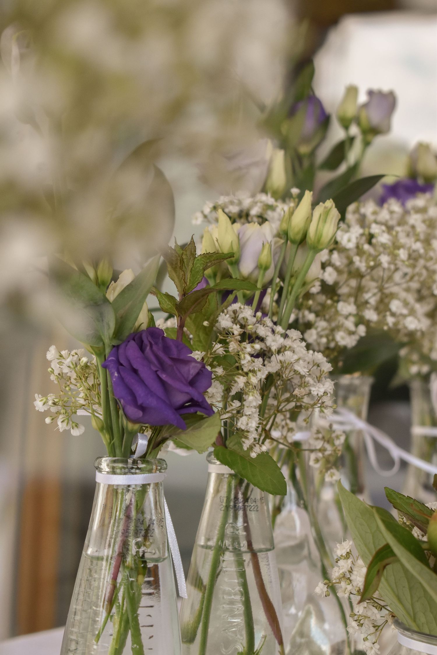 Purple and white flowers arranged in clear glass bottles with delicate baby's breath accents.