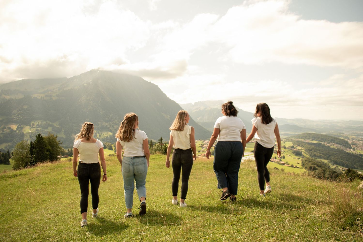 Friends walking hand in hand through a mountain meadow at sunset.