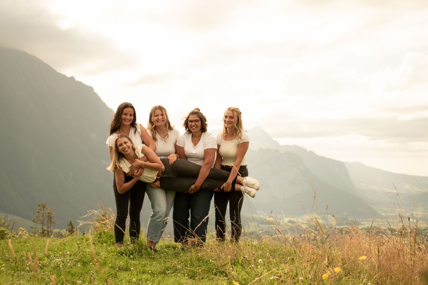 Group of friends posing together on a grassy hillside with mountains in the background.