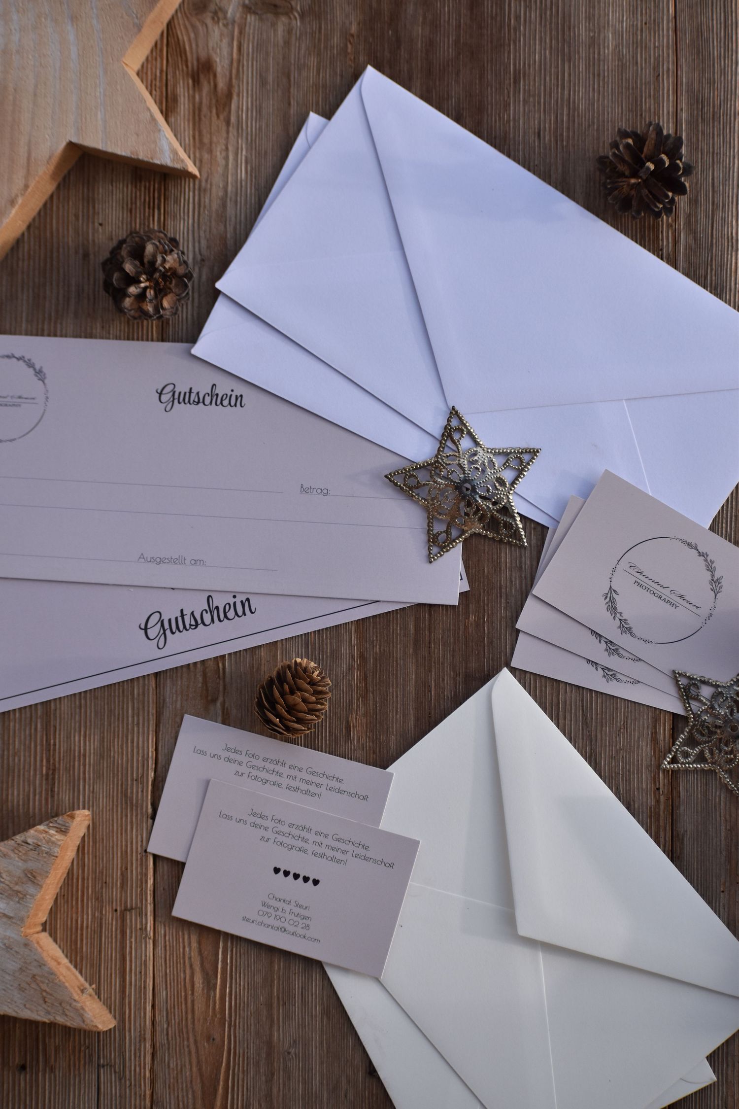 White envelopes and pine cones arranged on rustic wooden surface.