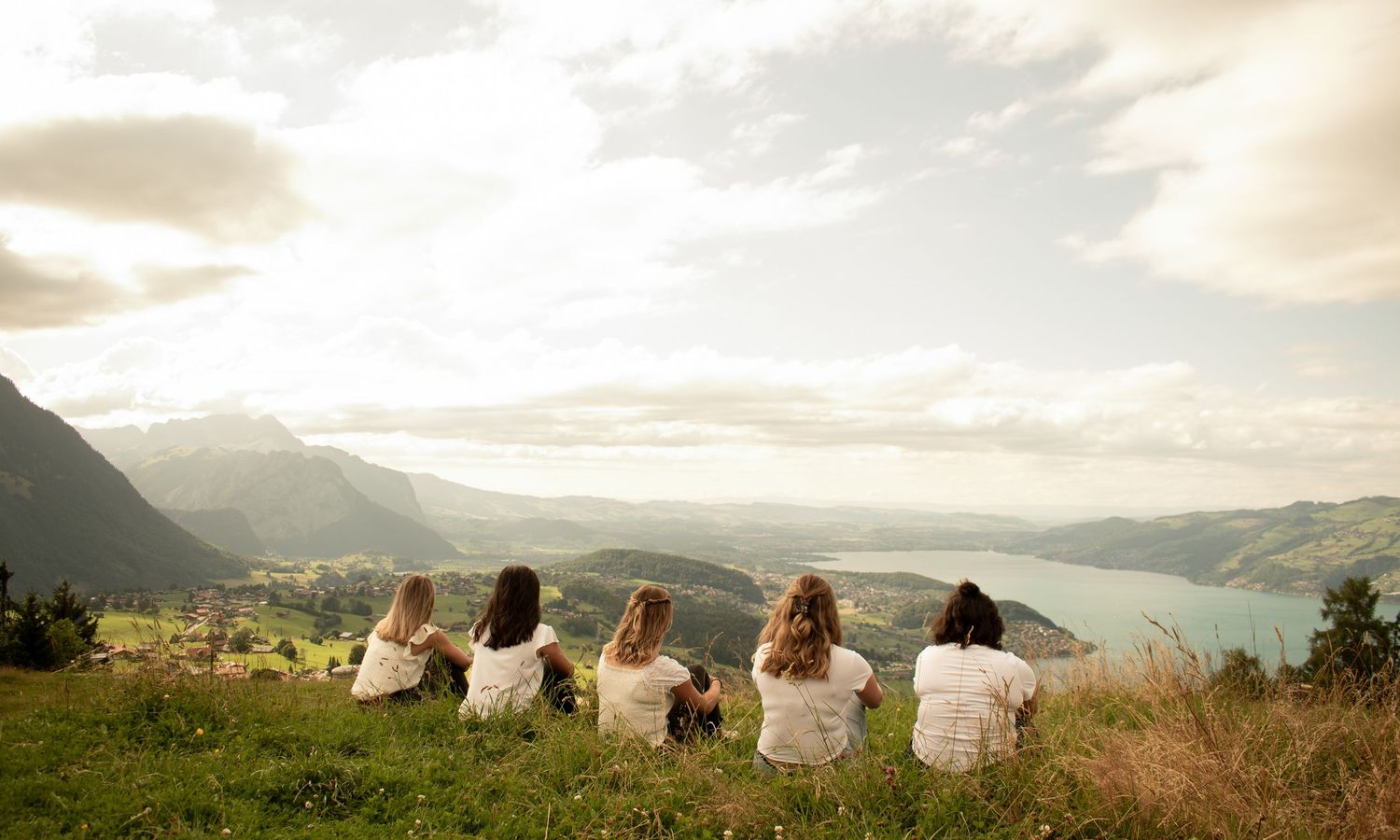 Friends relaxing on mountainside with panoramic valley views in golden light.