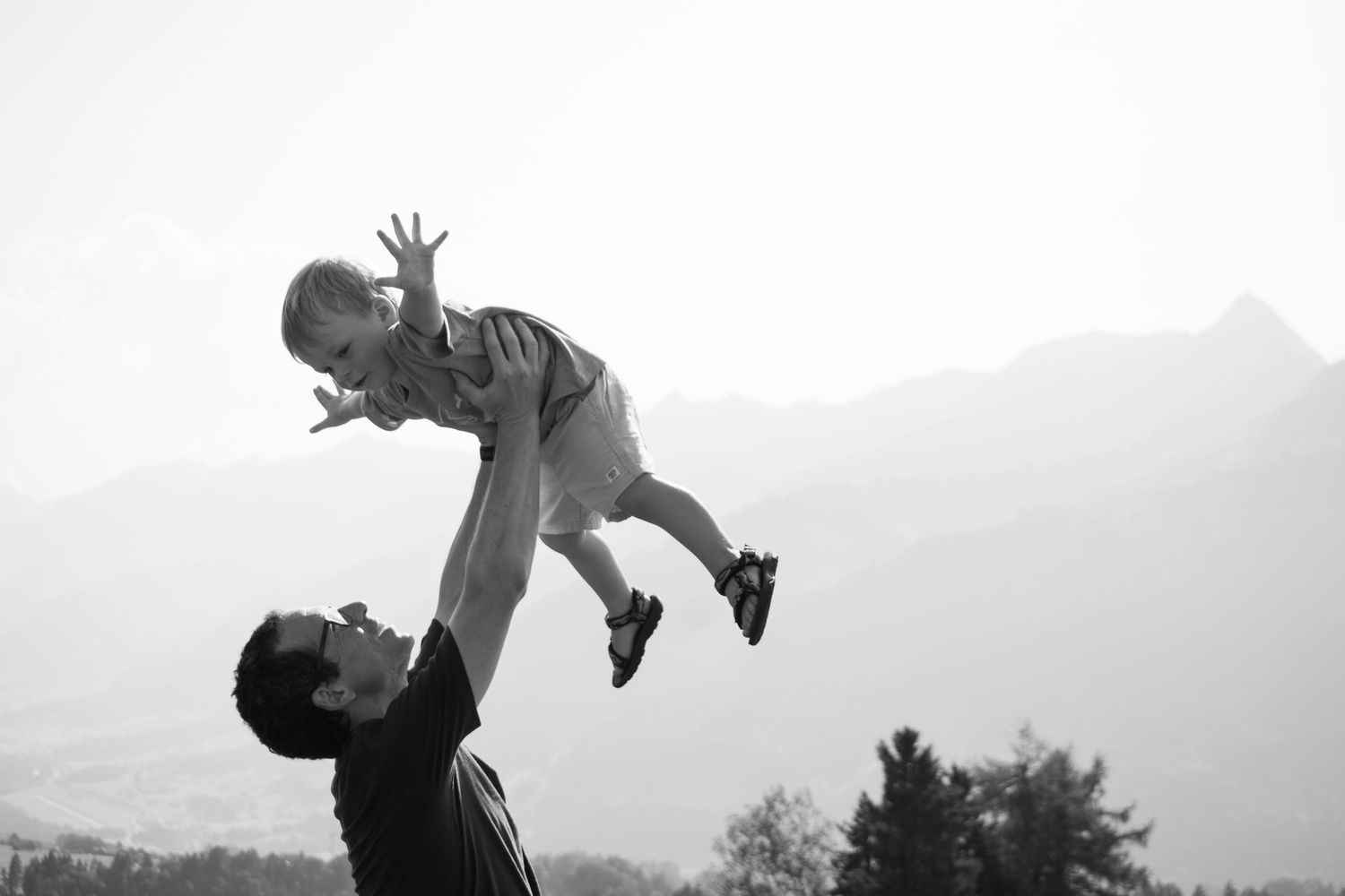 Silhouettes of people playing and lifting in a mountain field during sunset.