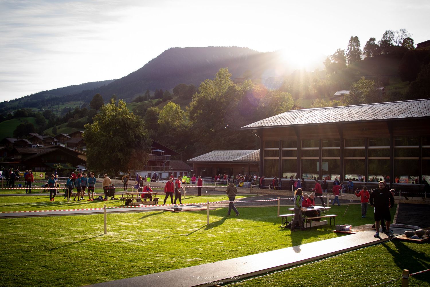 Panoramic view of a rustic outdoor venue at sunset with picnic tables and mountain backdrop.