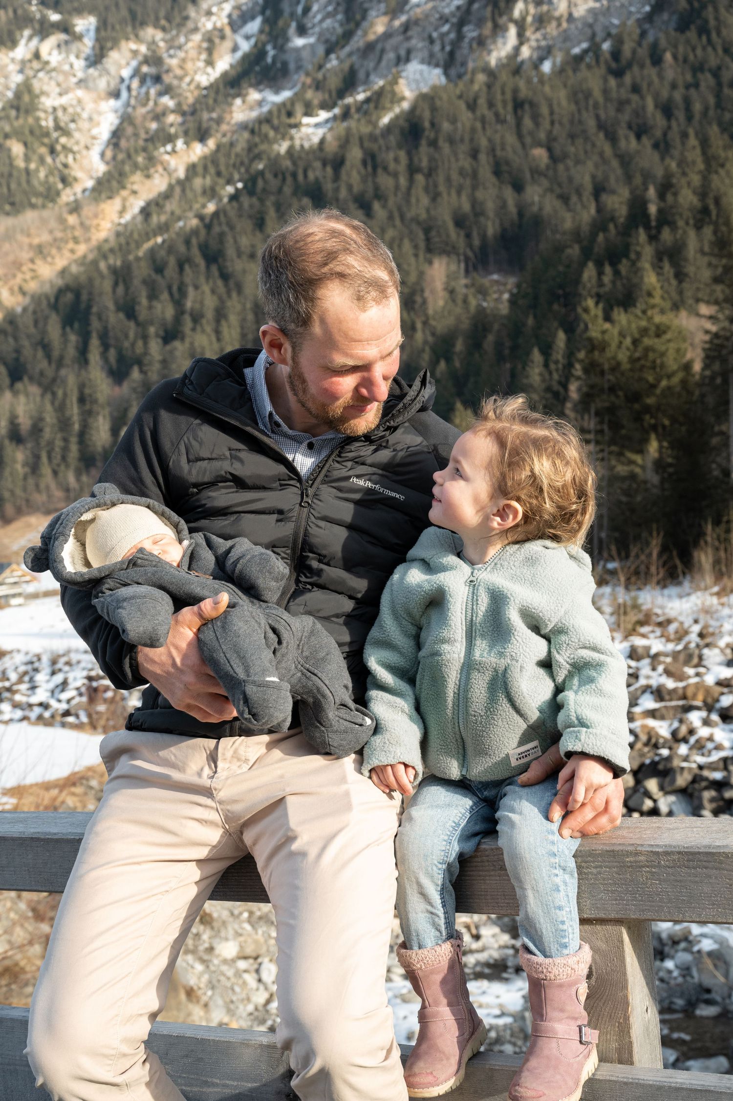 Family sharing a tender moment on a bench with snowy mountains in the background.