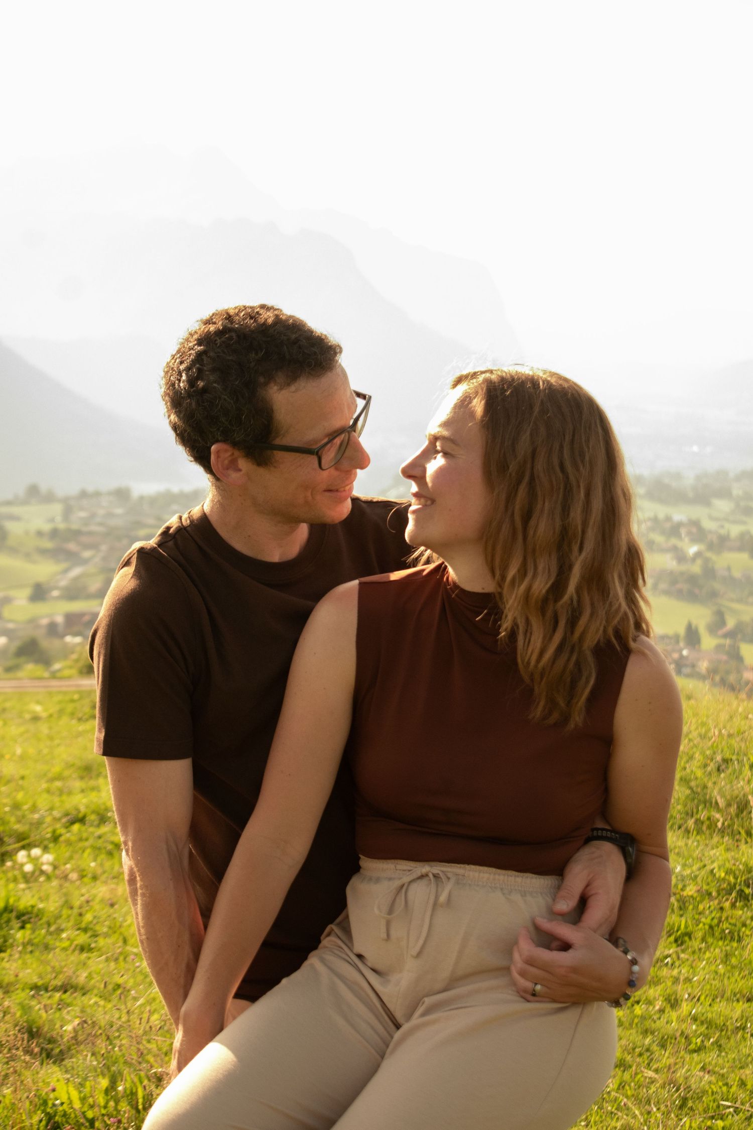 Romantic couple embracing in golden sunlight on hilltop meadow.