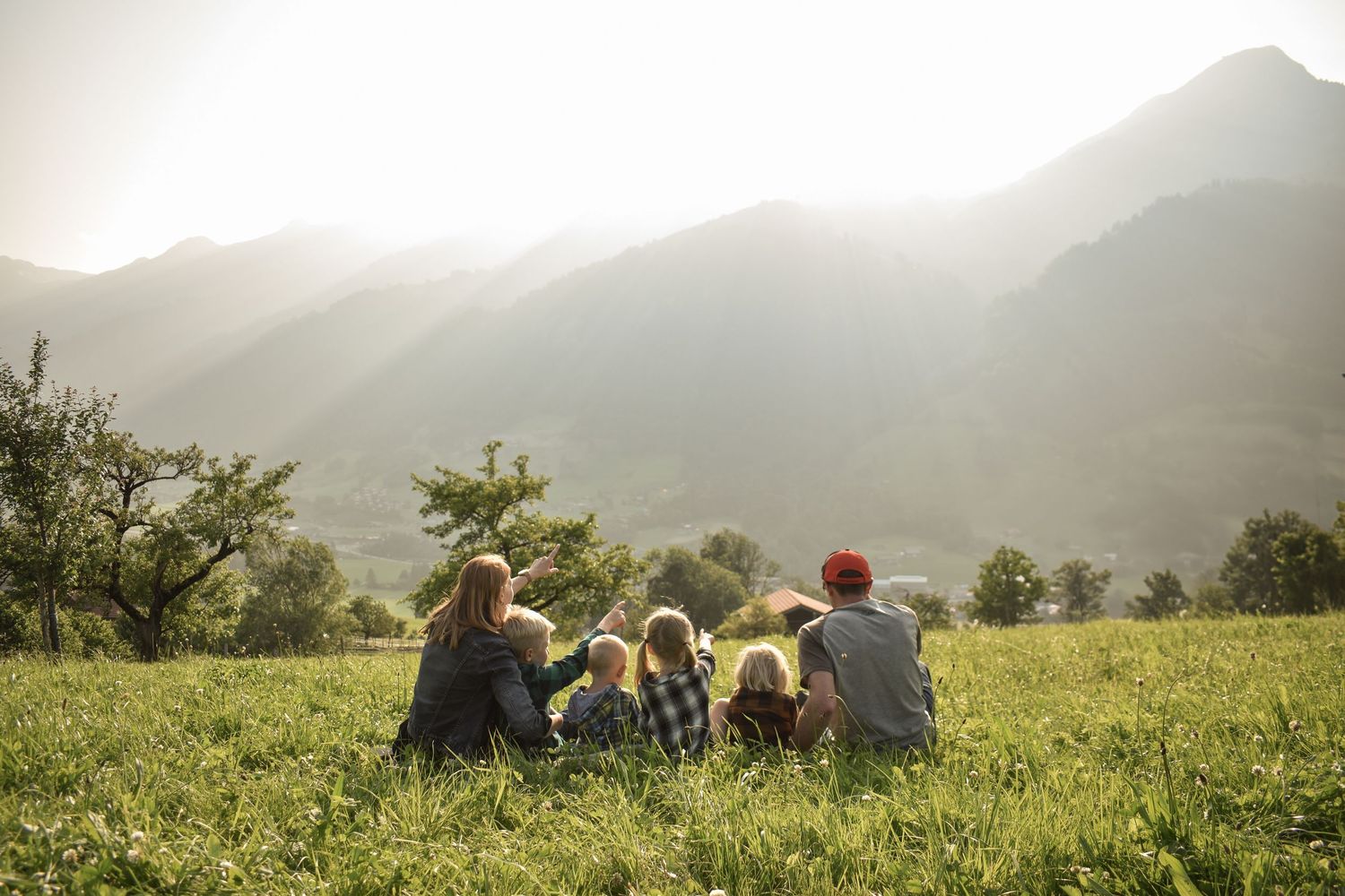 A group sits together on a hillside overlooking a scenic mountain landscape at sunset.