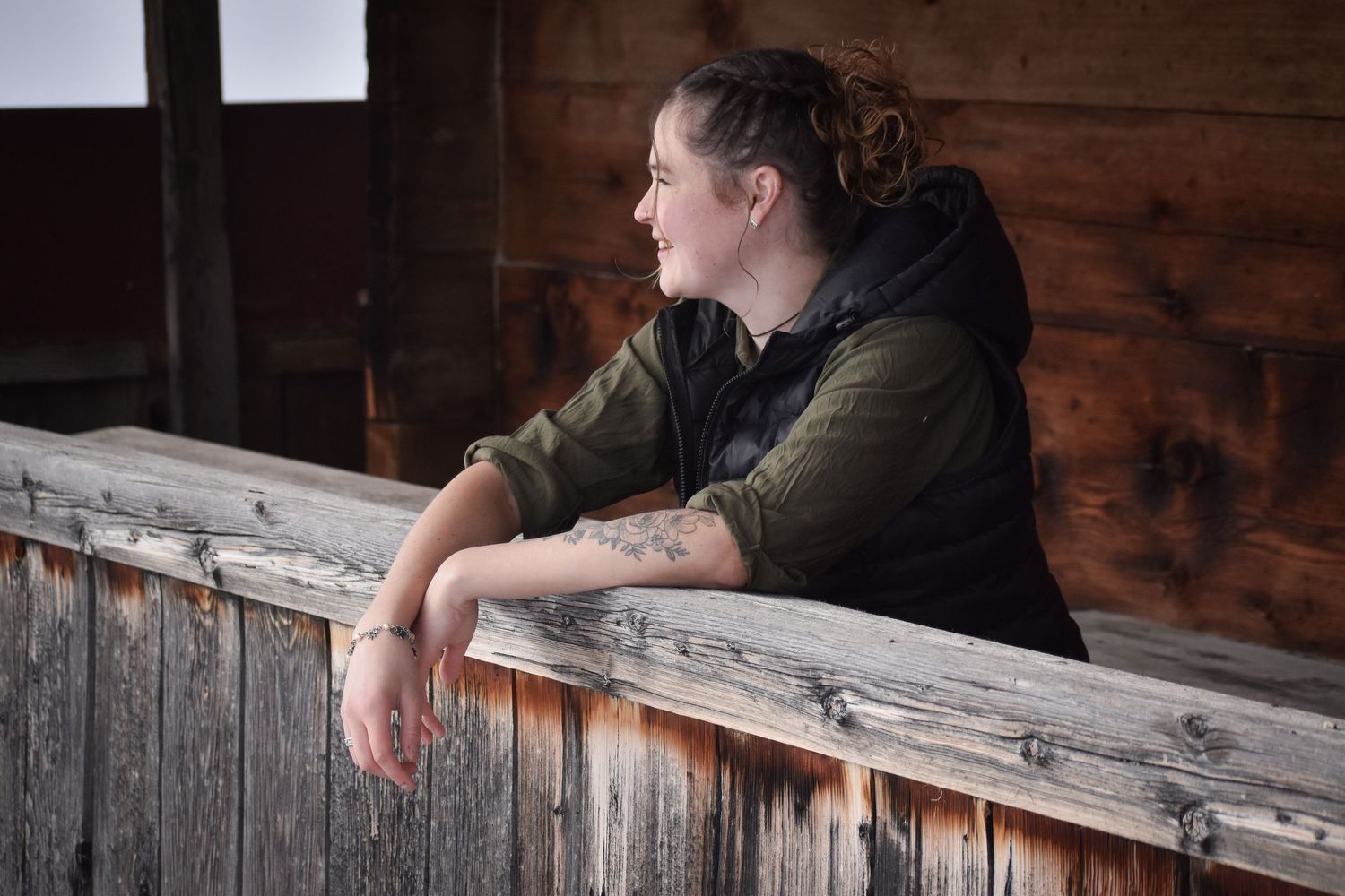 Person leaning on rustic wooden railing inside barn or cabin interior.