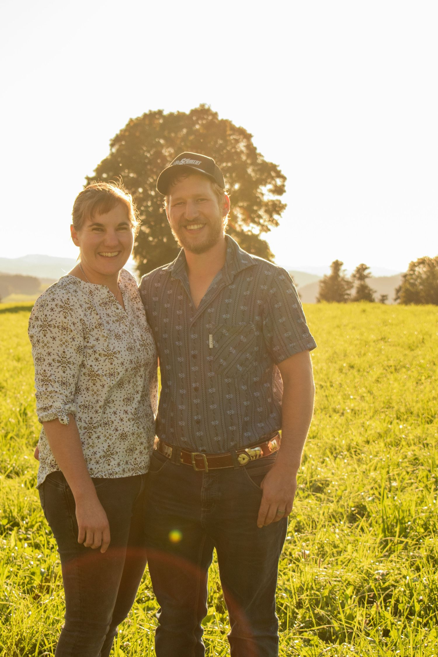 Couple posing together in a sunlit yellow field during golden hour.