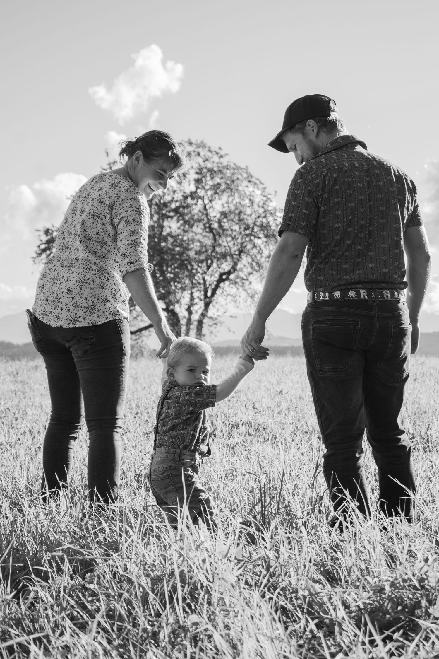 Family members standing together in a grassy field during golden hour with mountains in background.