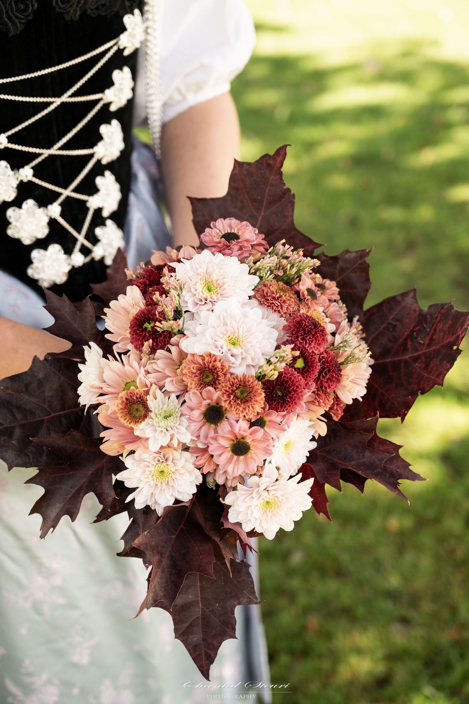 Wedding bouquet with pink and white flowers surrounded by dark burgundy maple leaves.