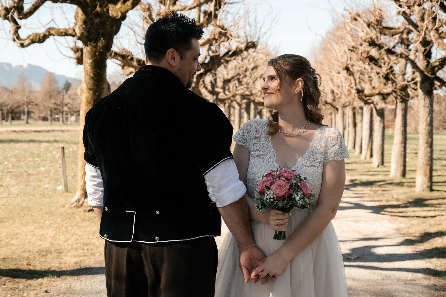 A couple in wedding attire shares romantic moments in a rustic orchard setting during golden hour.