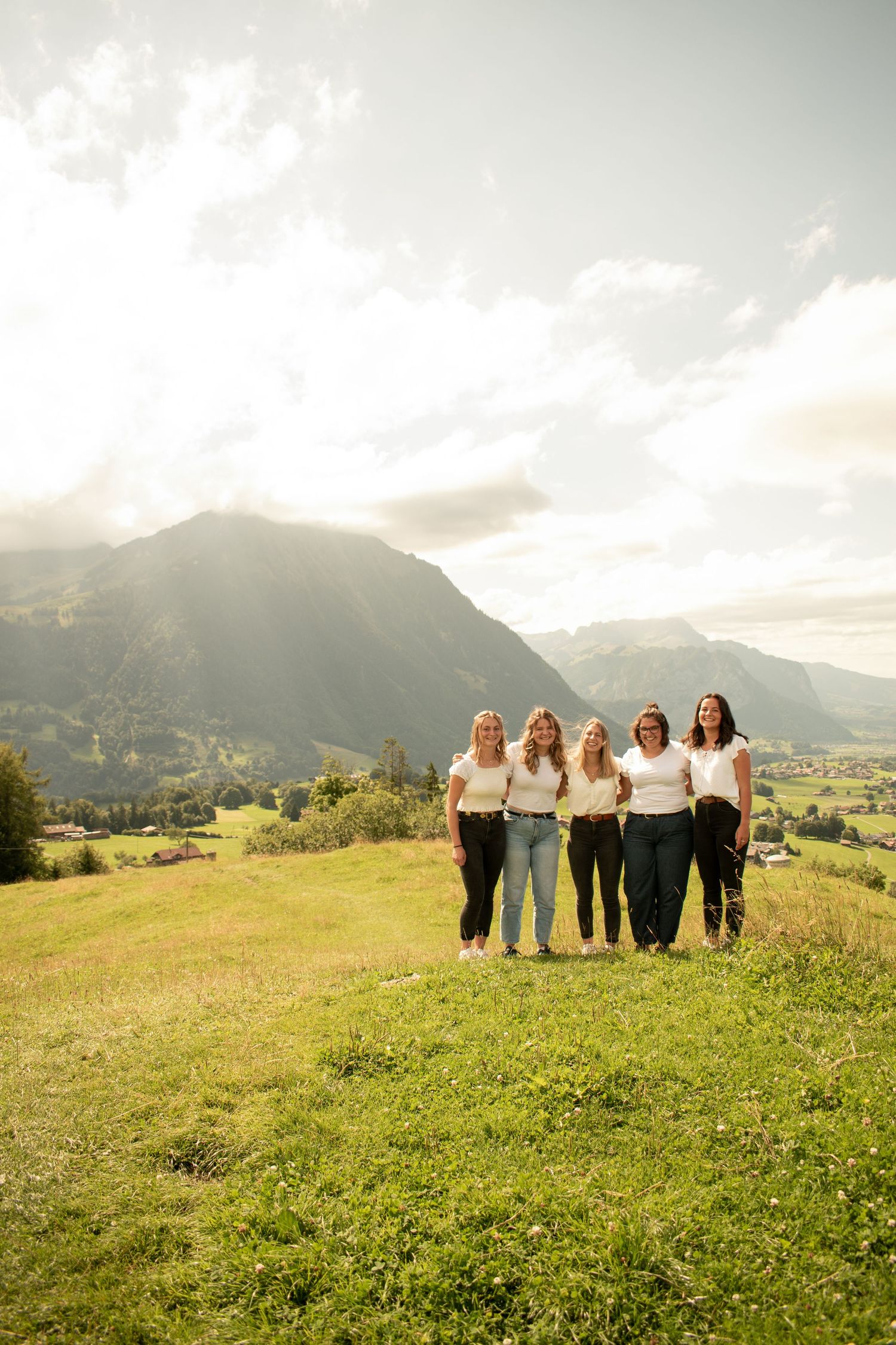 Group posing on hillside meadow with dramatic mountain backdrop.
