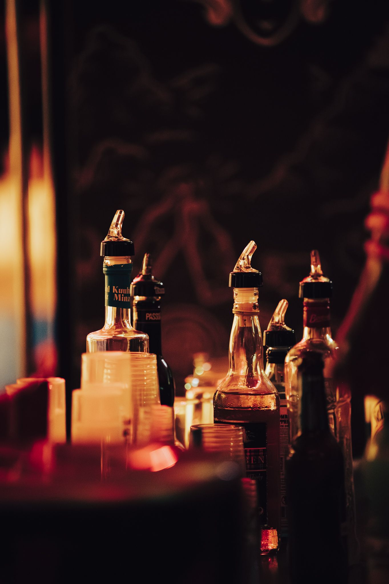 Dimly lit bar bottles with pourers glowing warmly in moody amber light, creating an atmospheric nightlife scene.