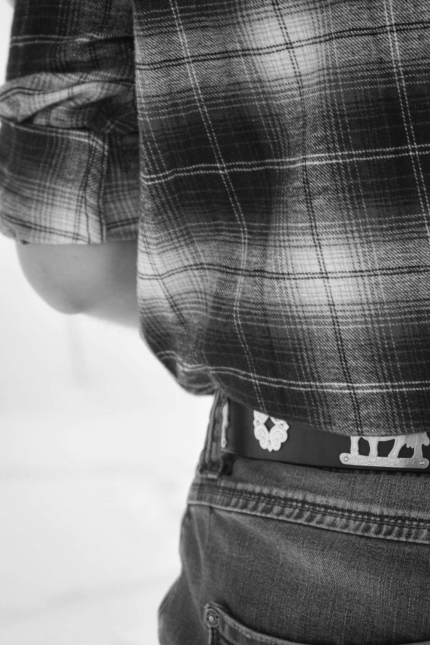 Close-up detail of plaid shirt and jeans with belt against monochrome background.