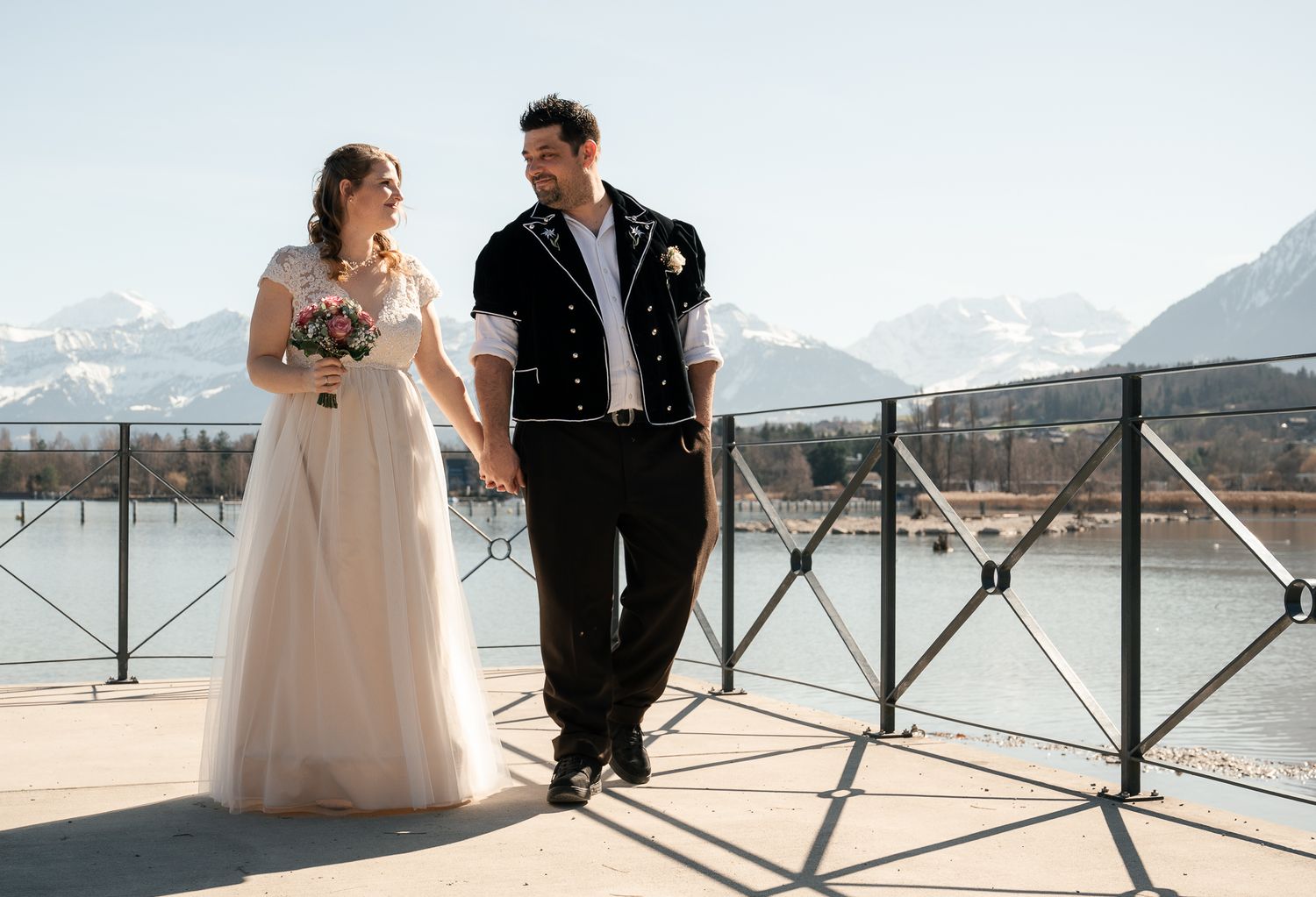 A couple in wedding attire poses together on a scenic mountain overlook with panoramic views in the background.