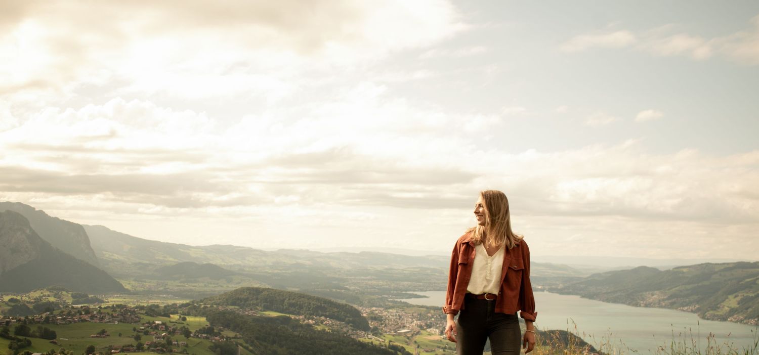 Person in rust-colored jacket gazes at mountain valley vista during golden hour.