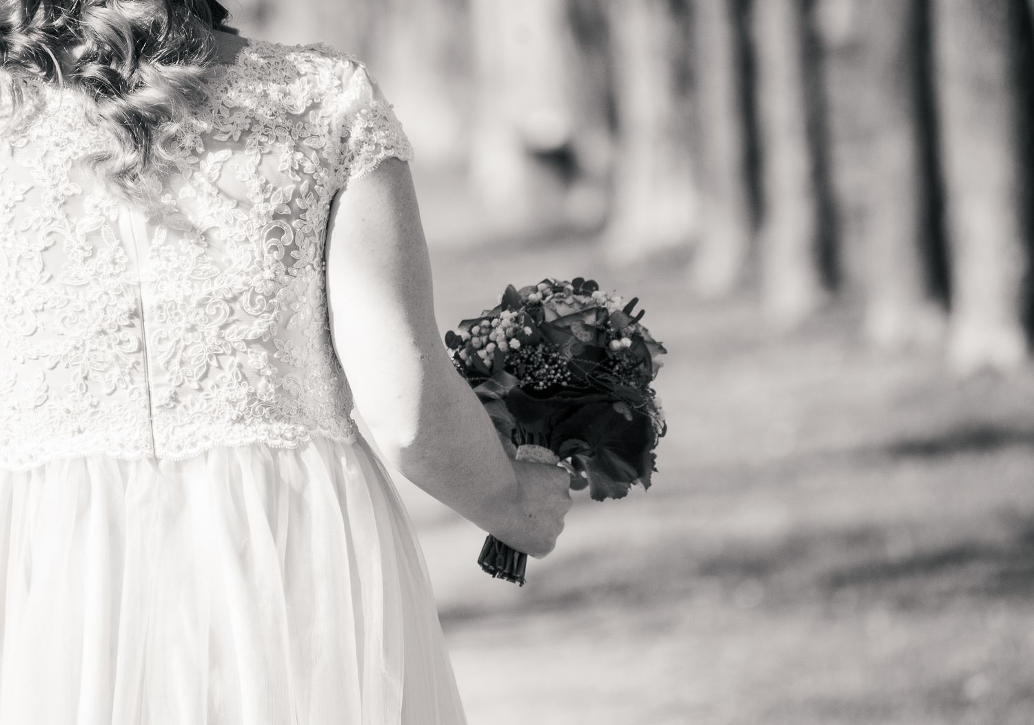 Black and white wedding photo showing couple dancing together in an elegant embrace on a sunny day outdoors.