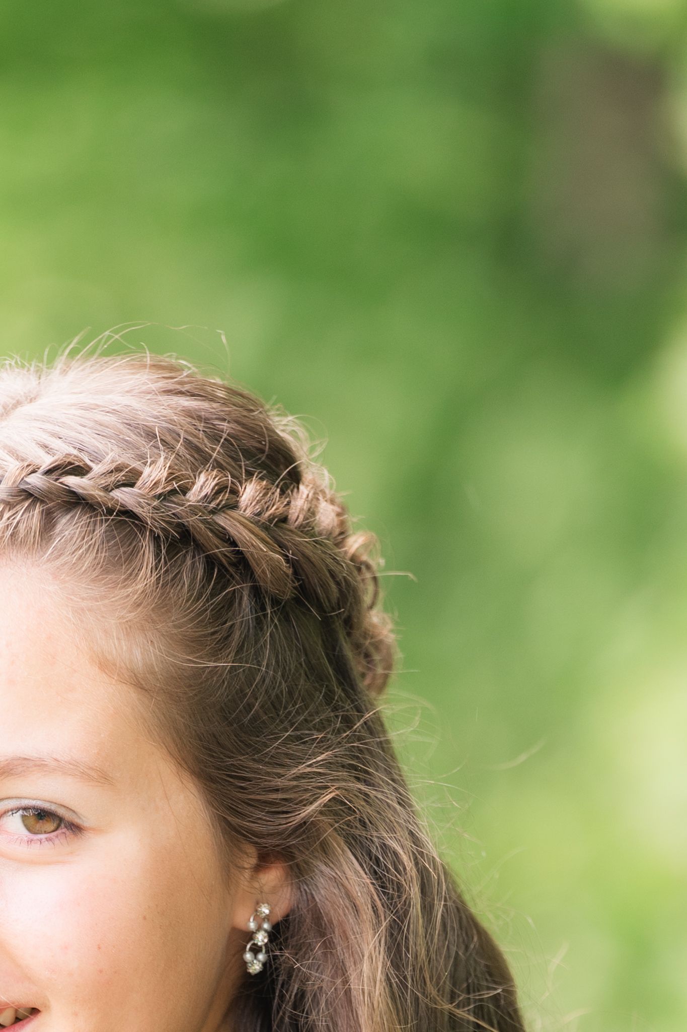 Close-up of elegant braided crown hairstyle with crystal earring on young woman outdoors.