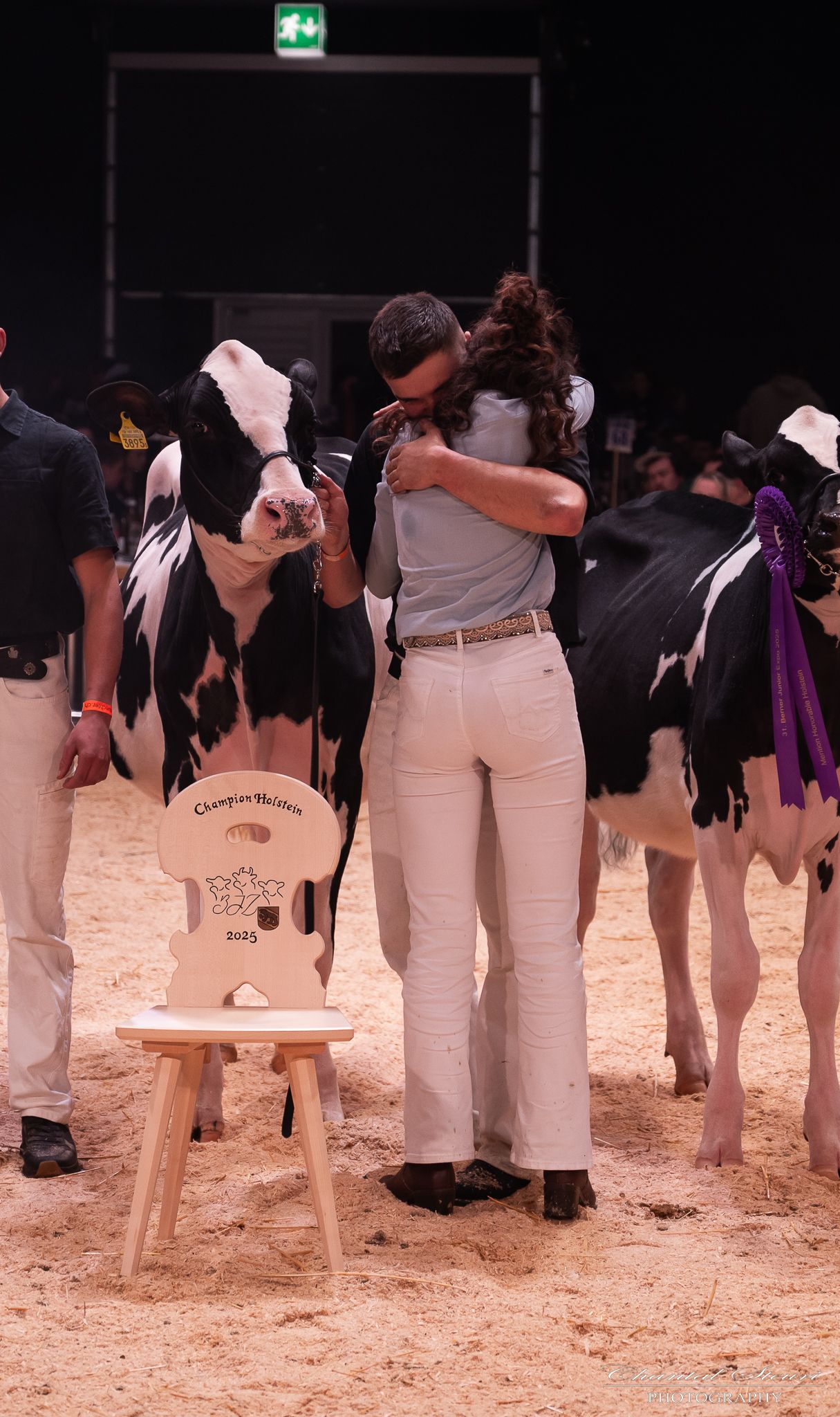 People in white pants and dark tops standing in a line on sandy ground at an indoor event.