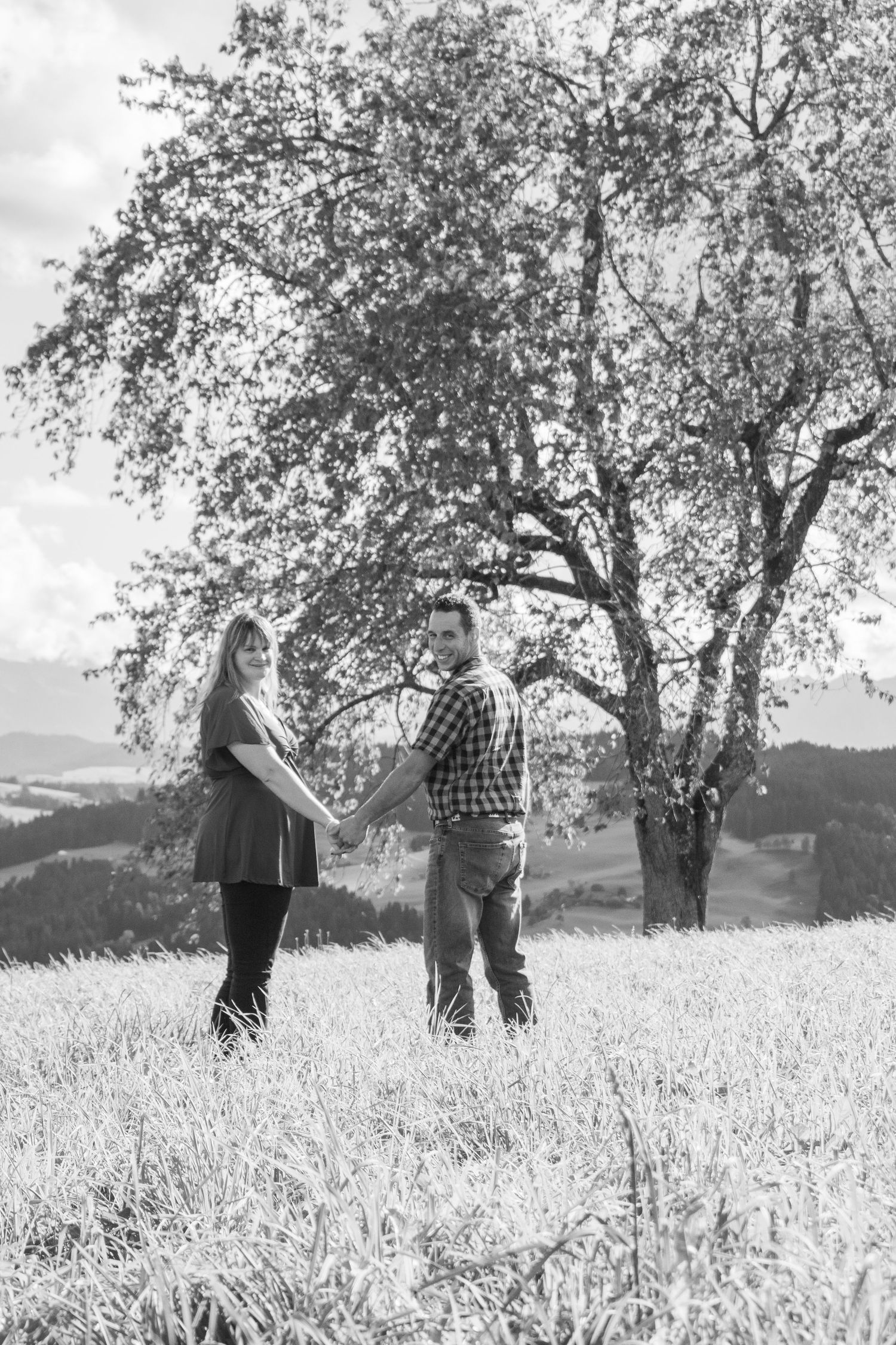 Black and white series of a couple standing together under a large tree in a field.