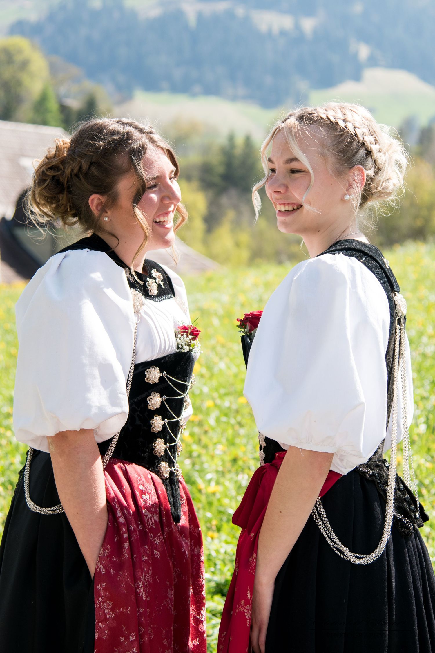 Two women in traditional Bavarian dirndl dresses standing in alpine meadow.