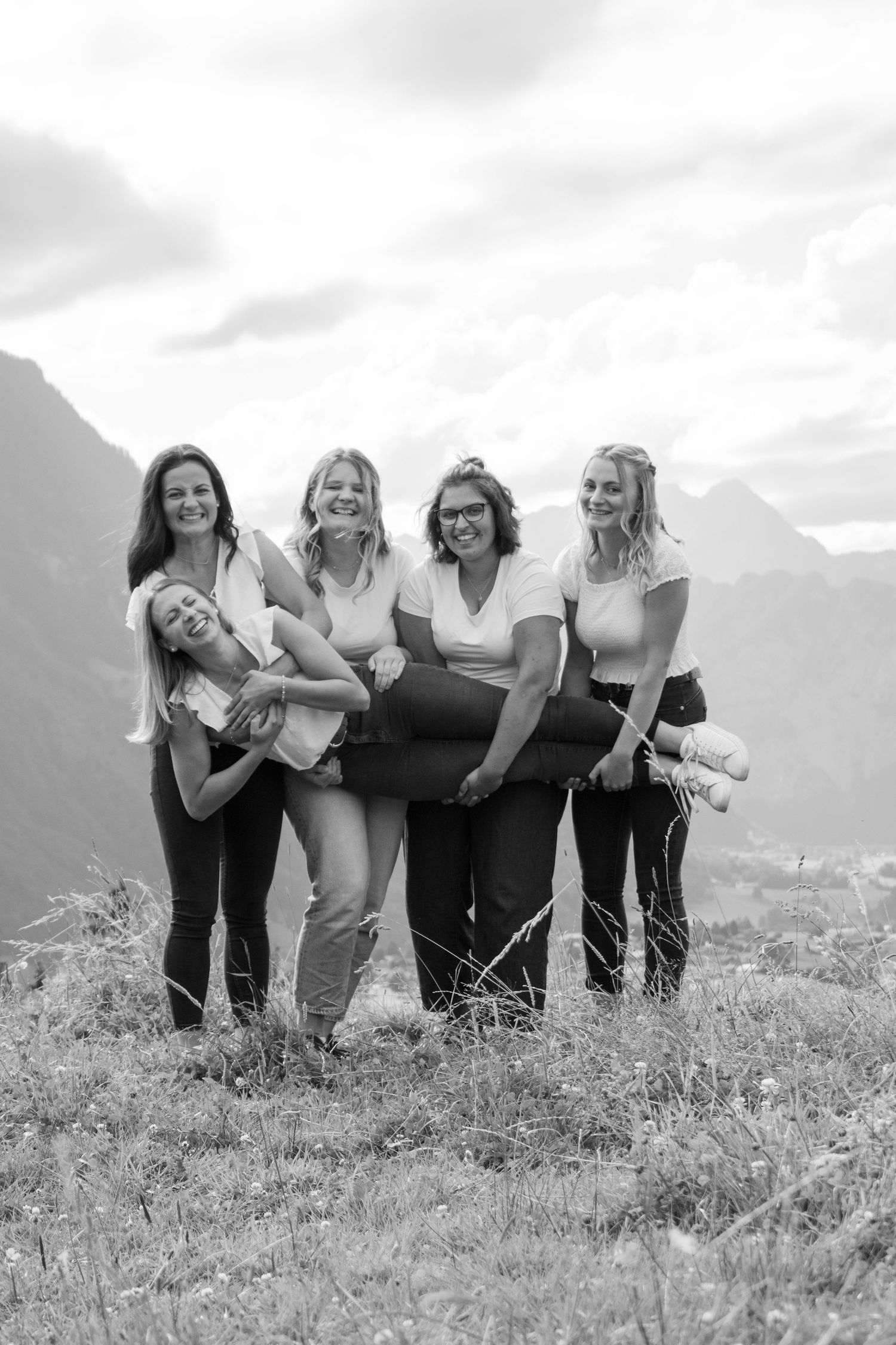 Black and white photo of friends embracing and laughing together on a mountain overlook.