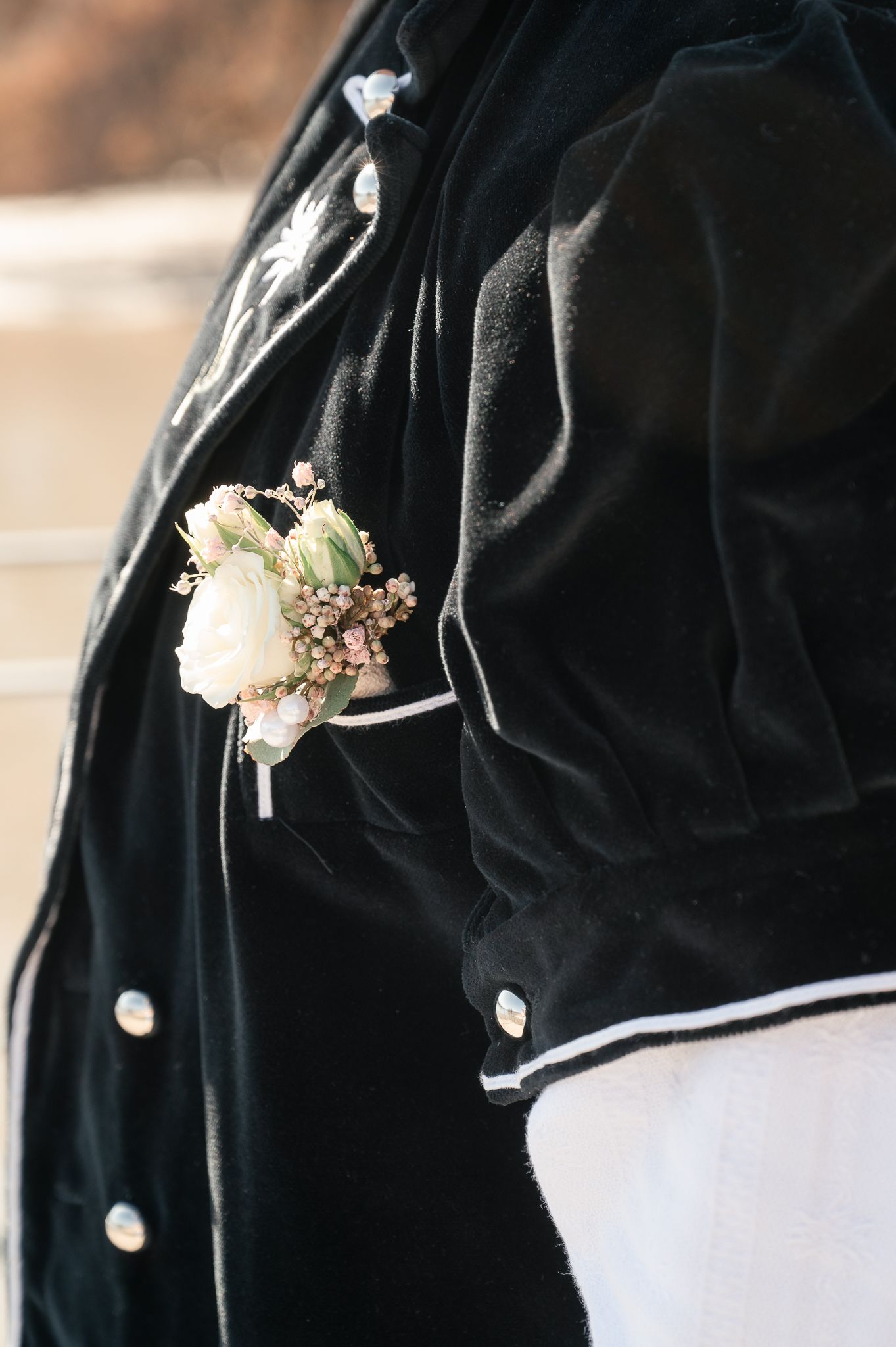 Close-up details of black suit jackets with white boutonniere flowers pinned to the lapels at a formal event.